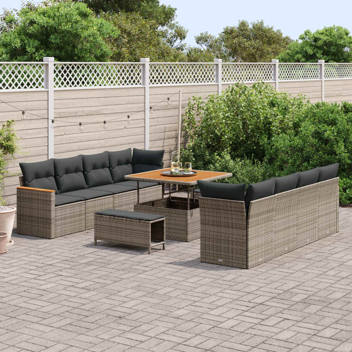 Geflochtenes Outdoor-Möbelset mit grauen Kissen auf einer Pflasterterrasse.