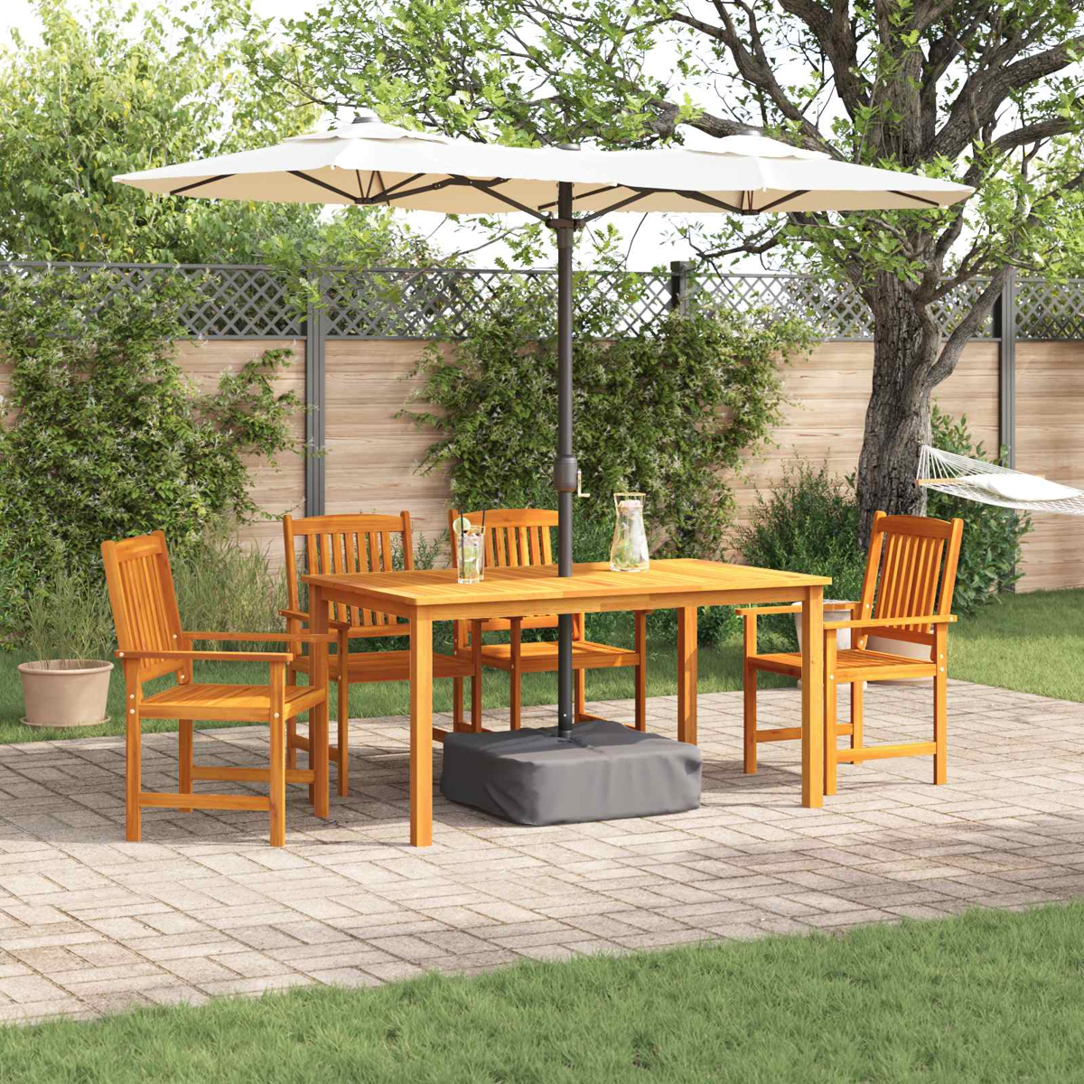 Holztisch und -stühle unter großem Sonnenschirm auf Terrasse, mit Grün und Hängematte im Hintergrund.