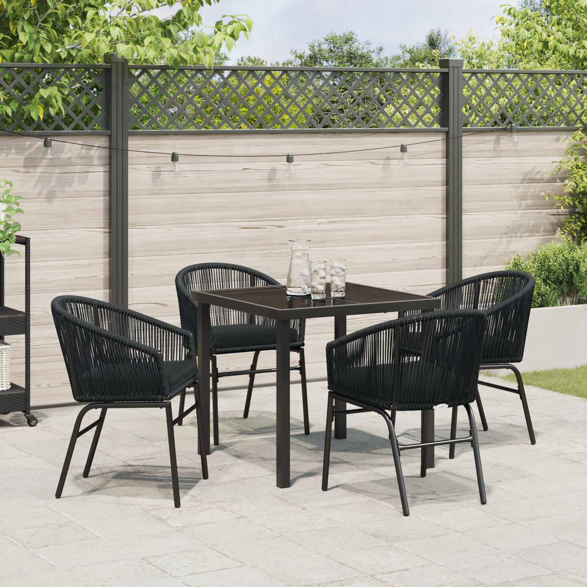 Ein rechteckiger Tisch und vier schwarze Korbstühle mit Kissen auf einer gefliesten Terrasse.