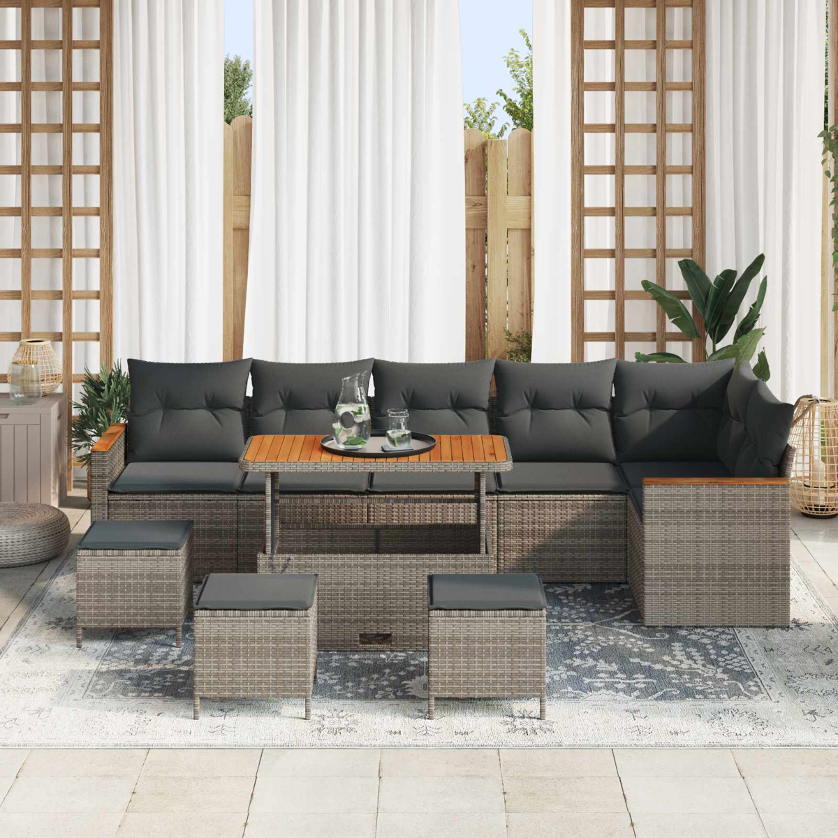 Graue Rattansofa-Ecke mit dunklen Kissen, Holztisch und Hockern auf einer Terrasse.