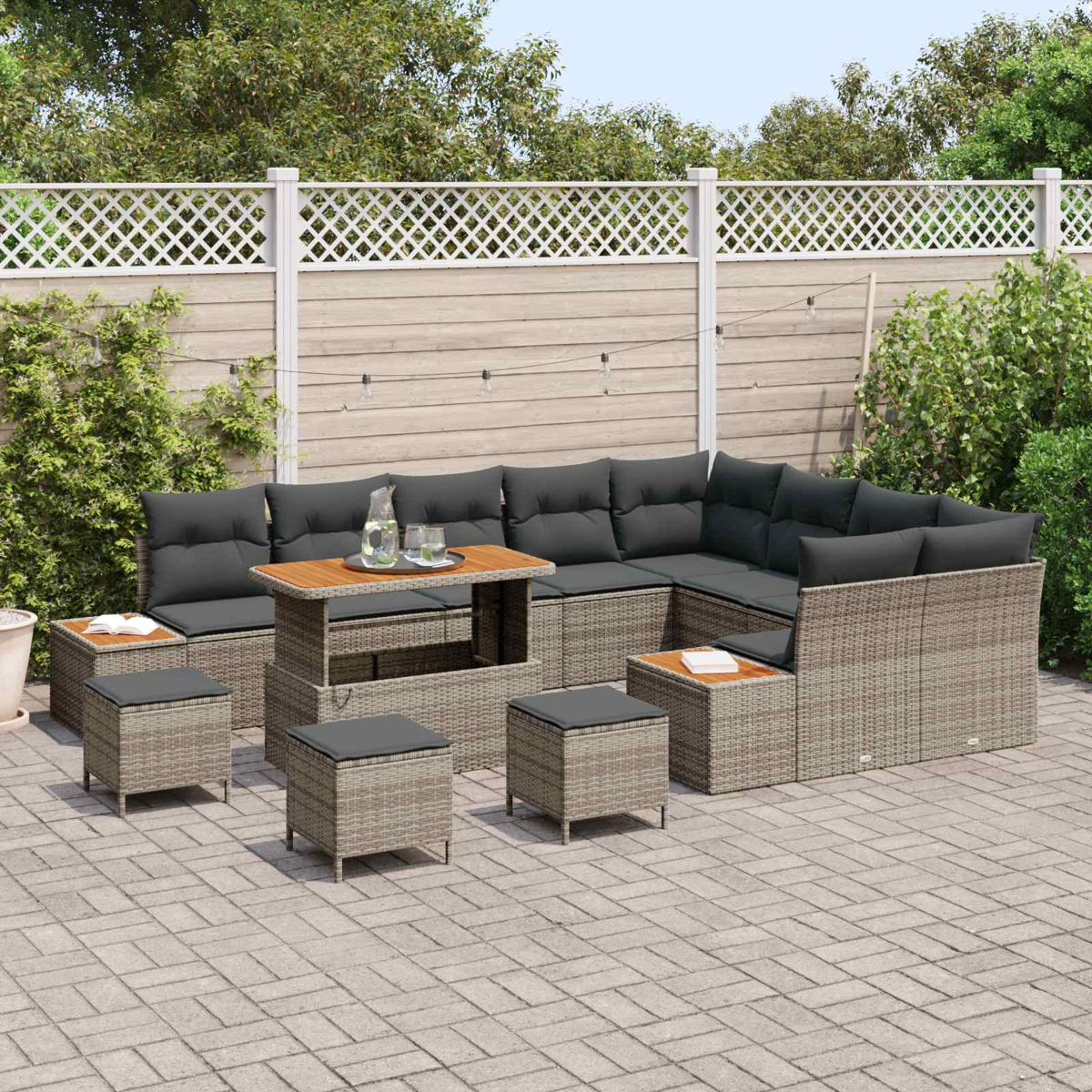 Graue Rattan-Lounge-Garnitur mit Tisch und Hockern auf gepflastertem Hof.