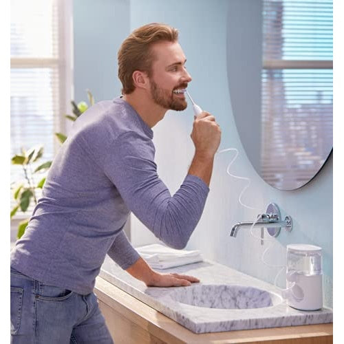 Uomo usa un idropulsore in un bagno con lavandino e rubinetto in marmo.