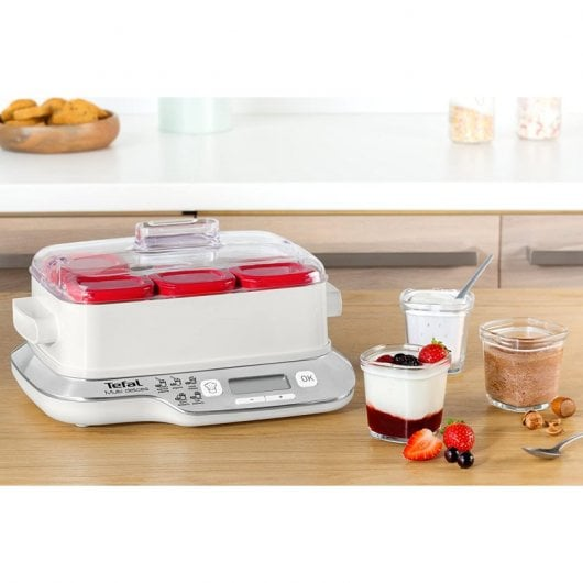 Una yogurtera blanca con recipientes rojos y vasitos de yogur con fruta.