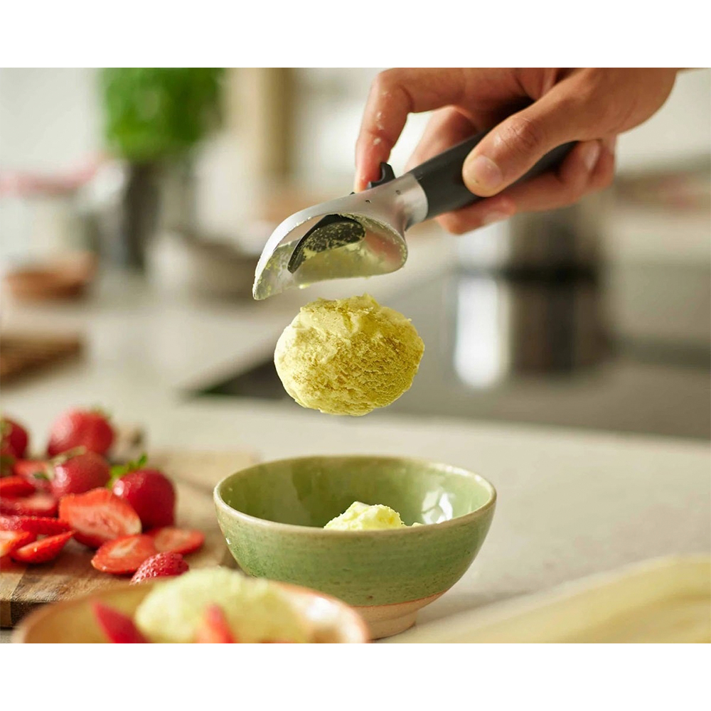 Una mano raccoglie una pallina di gelato giallo sopra una ciotola con un coppagelato.