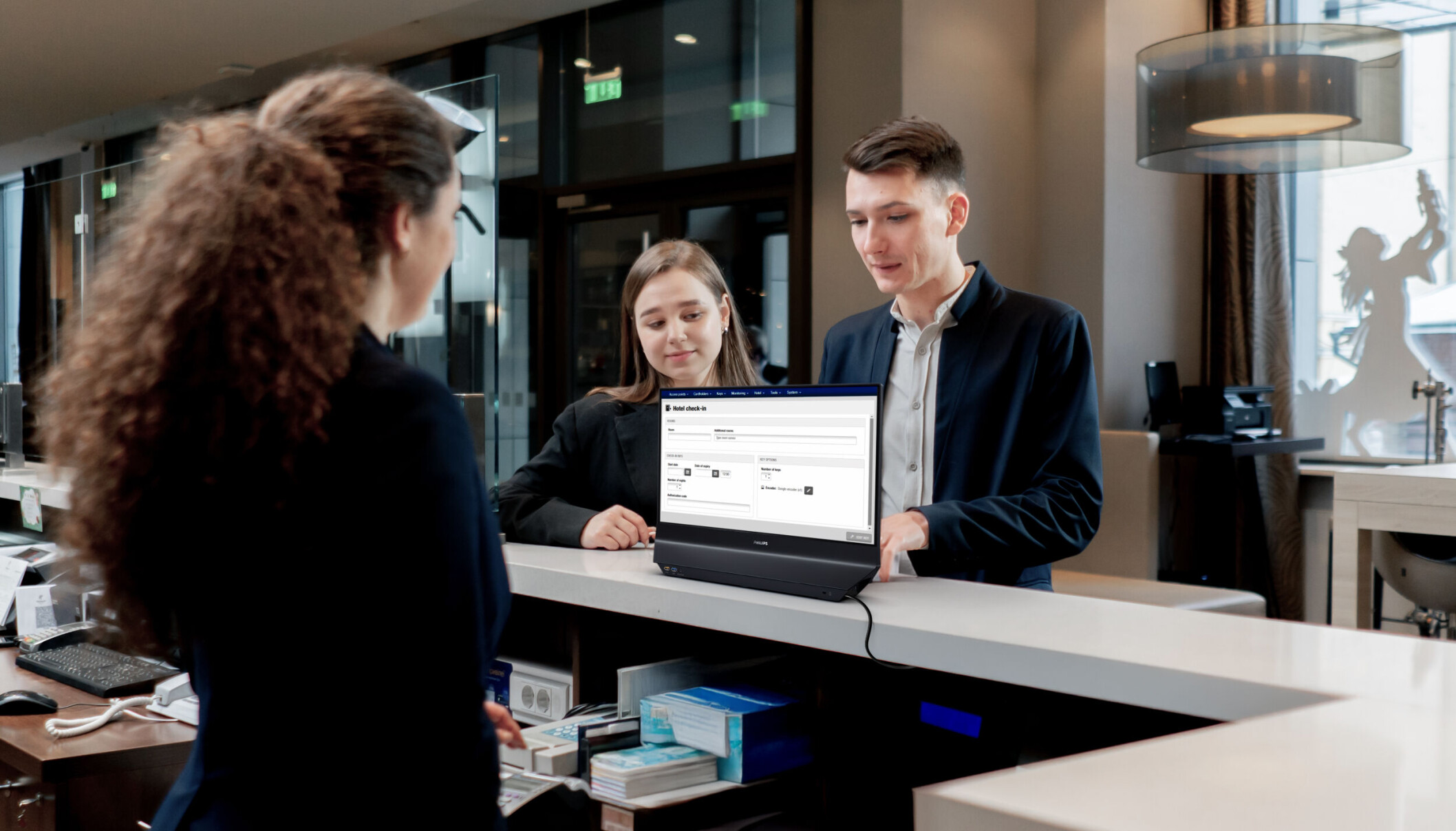 Un impiegato dell'hotel serve due ospiti a una scrivania con schermo.