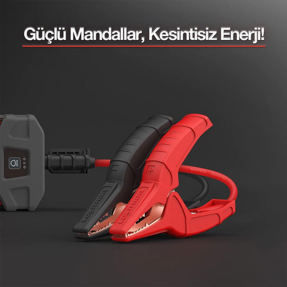 İki akü takviye kablosu mandalı, biri kırmızı, biri siyah; siyah kablo ve gri cihaz.