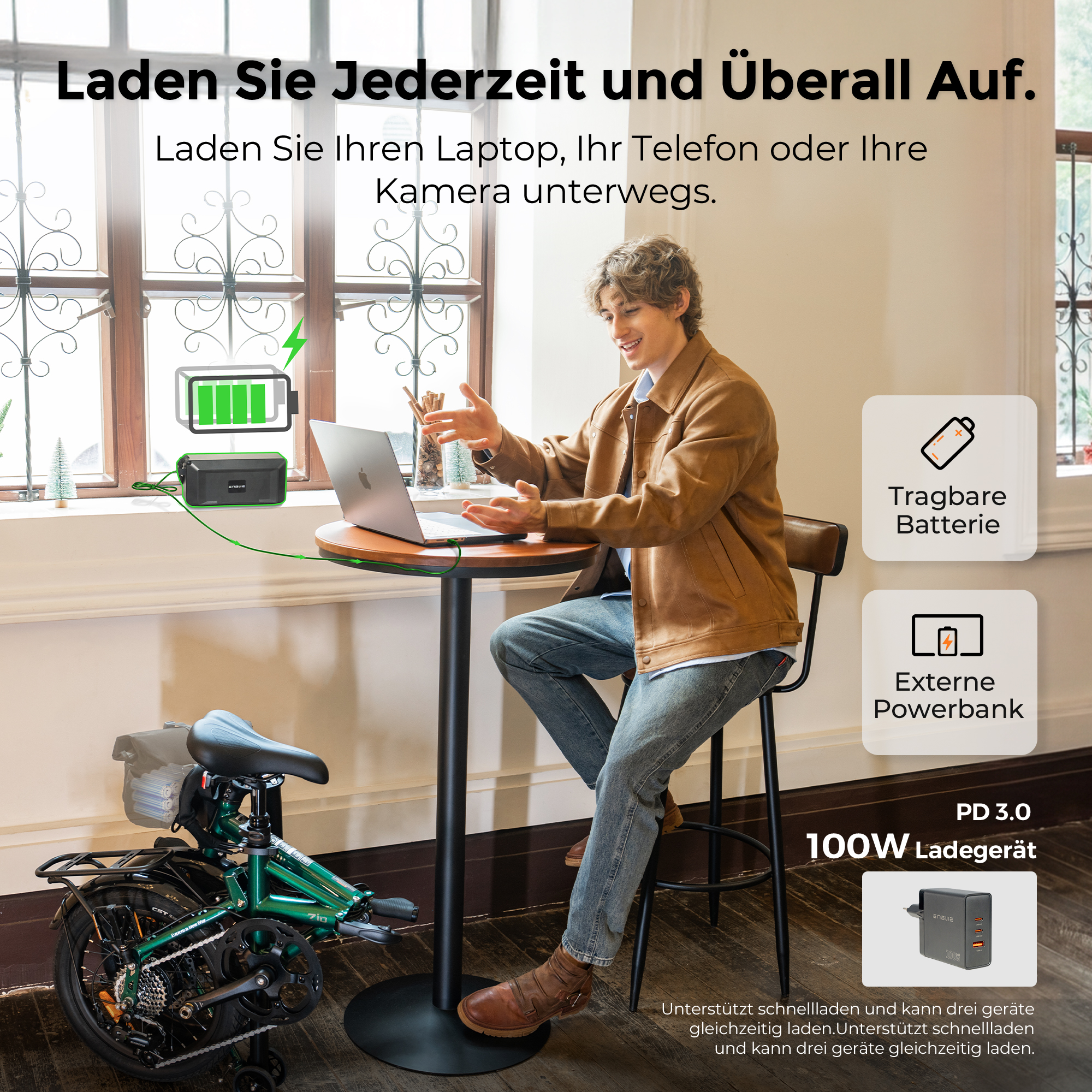Uomo seduto al tavolo con laptop, e-bike, caricabatterie, powerbank e batteria.