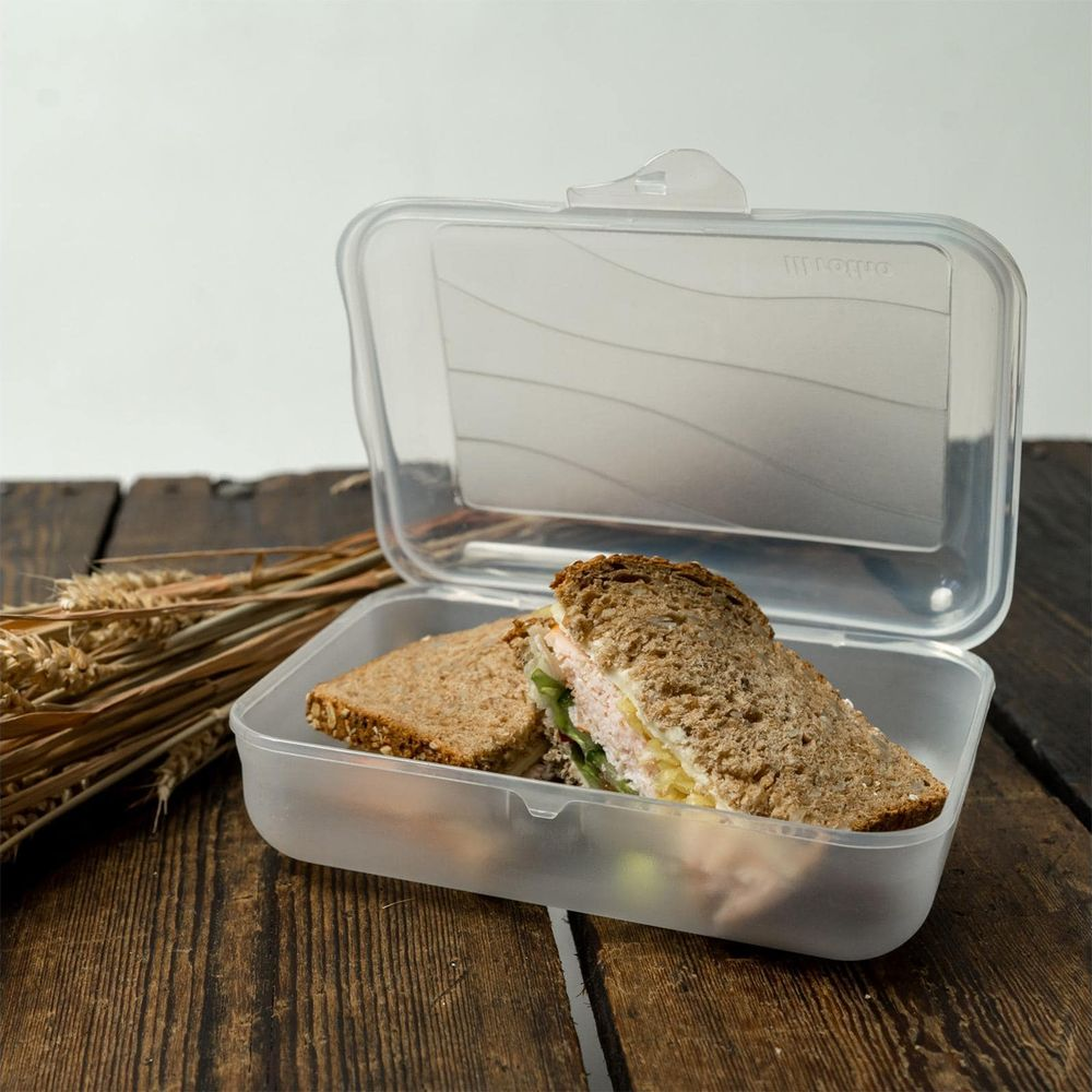 Otwarty przezroczysty pojemnik na lunch z dwoma kanapkami i kłosami pszenicy na drewnianym stole.