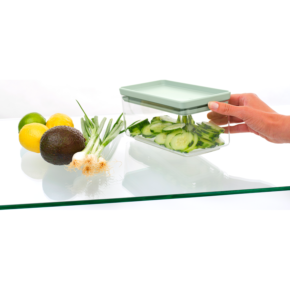 Mano che posiziona contenitore di cetrioli affettati vicino ad avocado, limoni, lime e cipollotti.