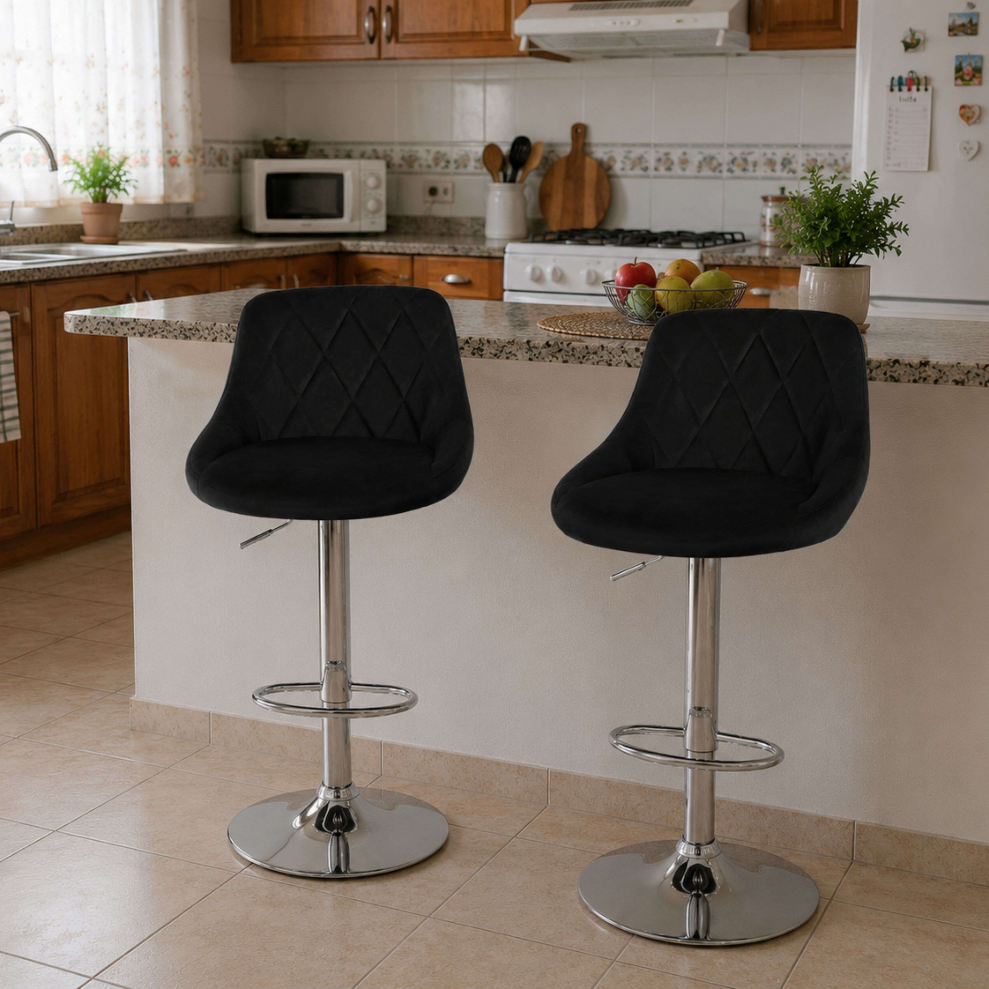 Dos taburetes de bar negros con base cromada delante de una encimera de cocina con frutero.