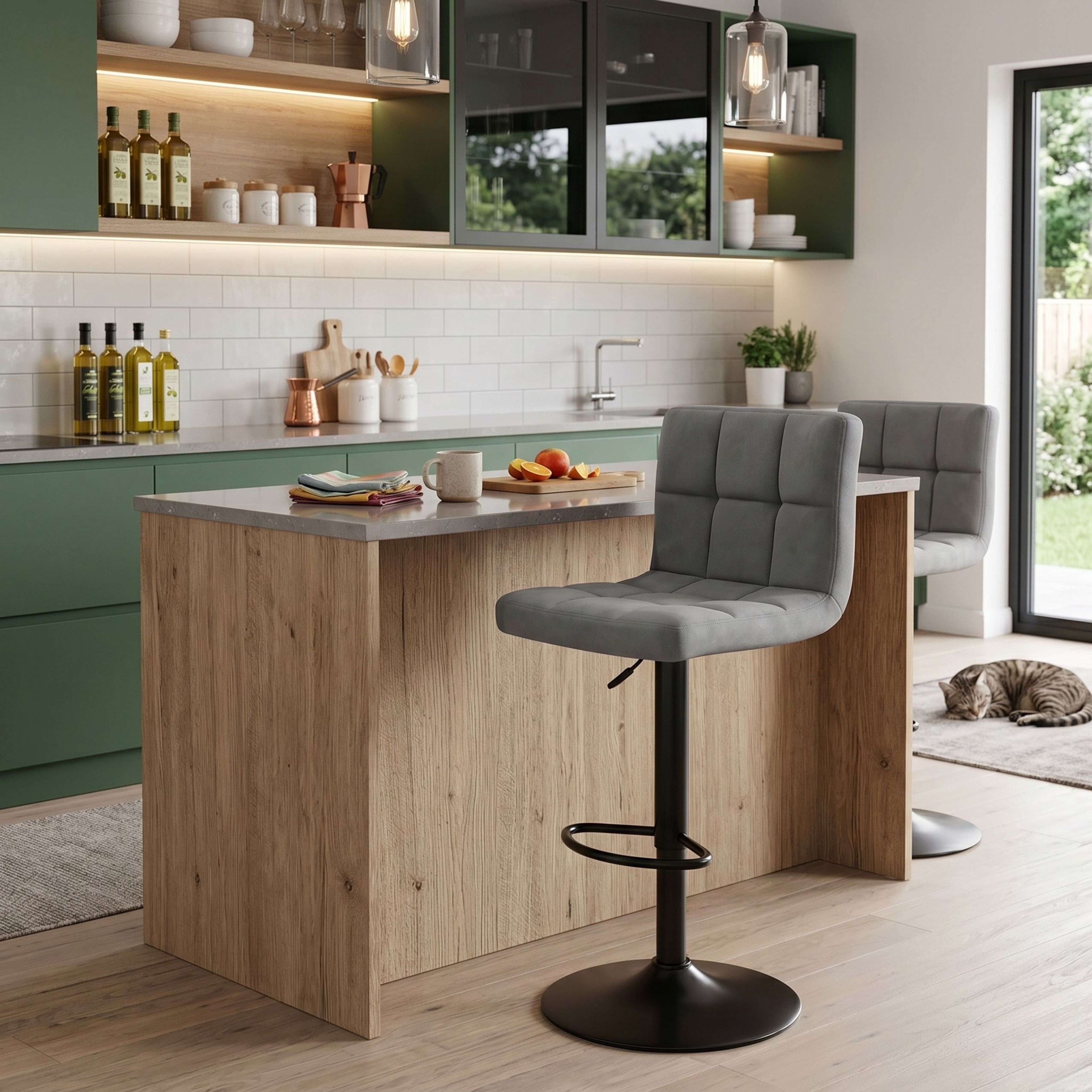 Cocina moderna con gabinetes verdes, detalles en madera, taburetes y gato.