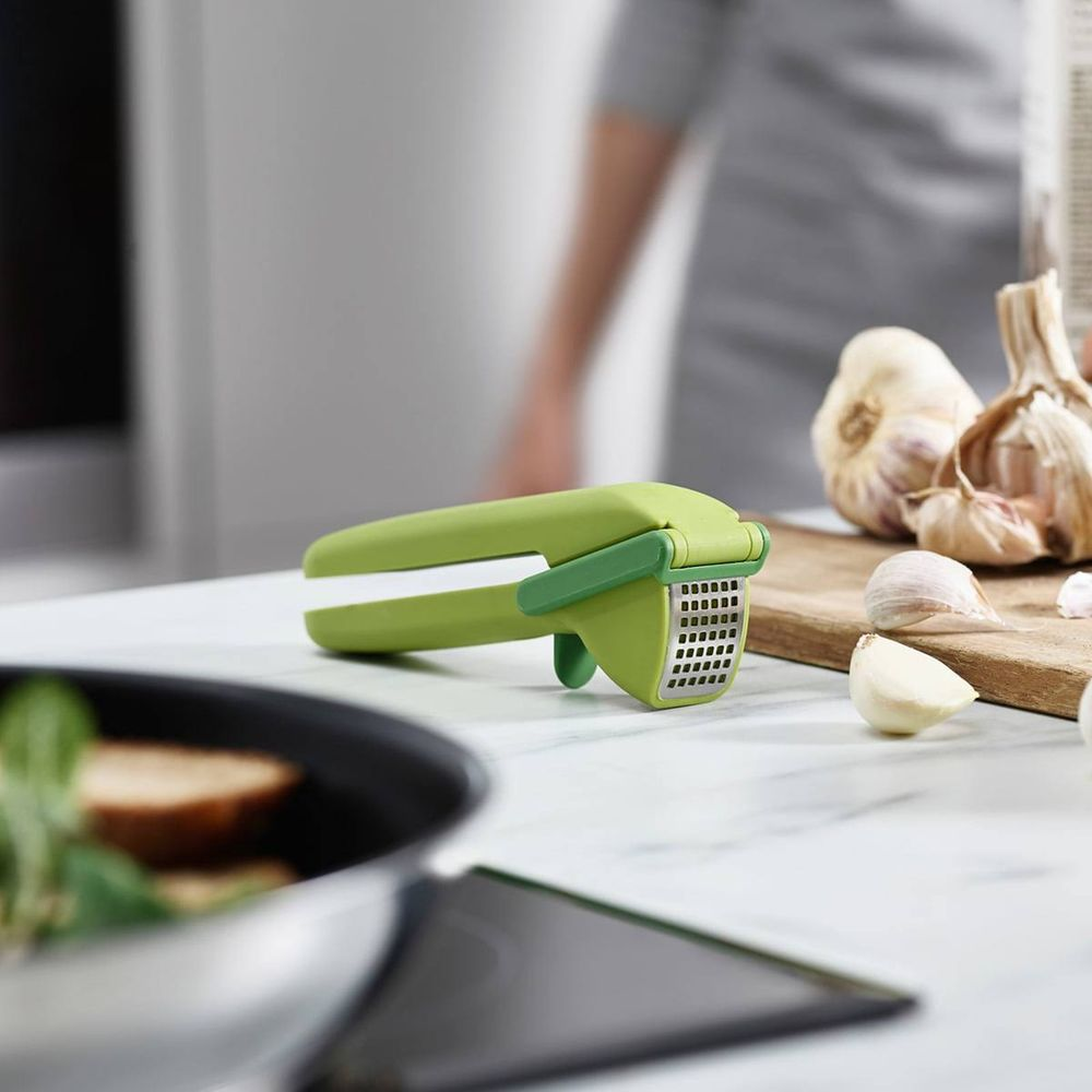 Schiacciapatate verde su un bancone da cucina con spicchi d'aglio.