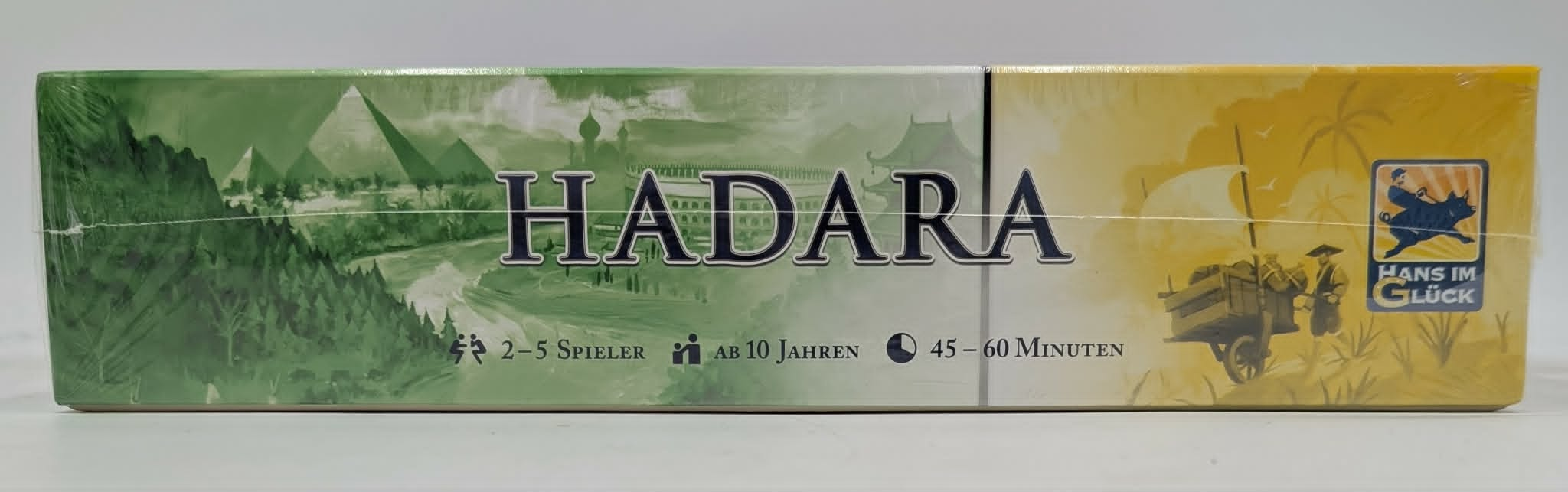 Brettspiel-Box mit „HADARA“ Schriftzug, grüne Landschaft links, gelbe rechts.