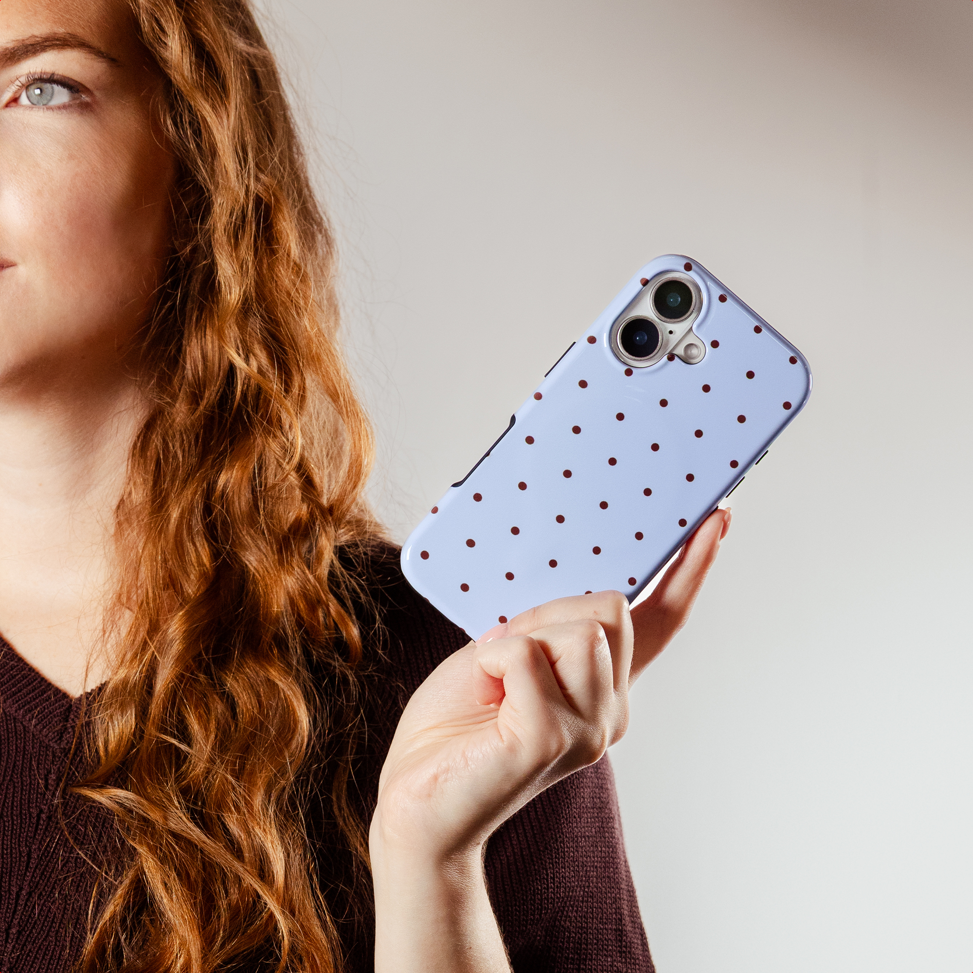 A woman with red hair holds a light blue phone with brown polka dots.