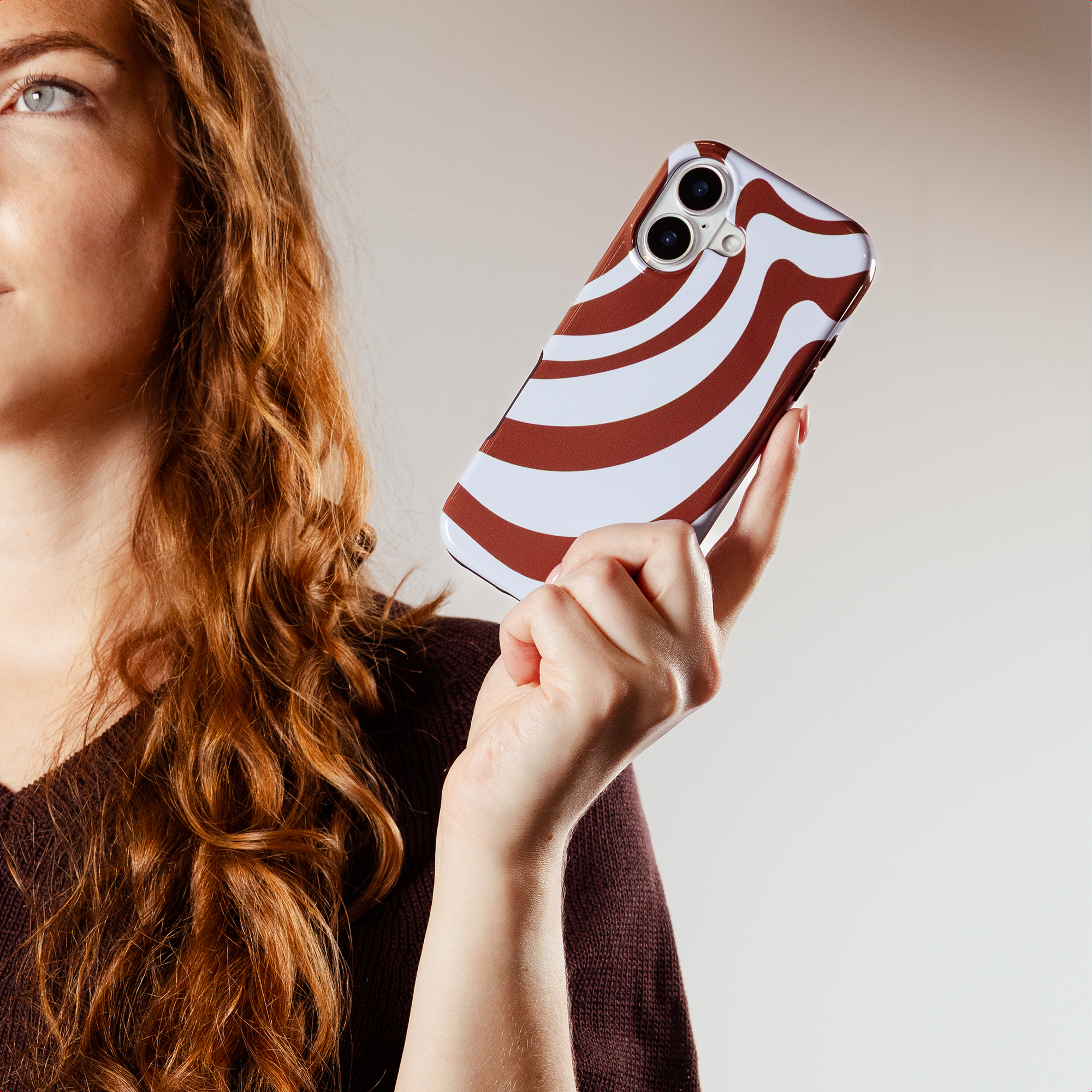 A woman with red hair holds a smartphone with a brown and white pattern.