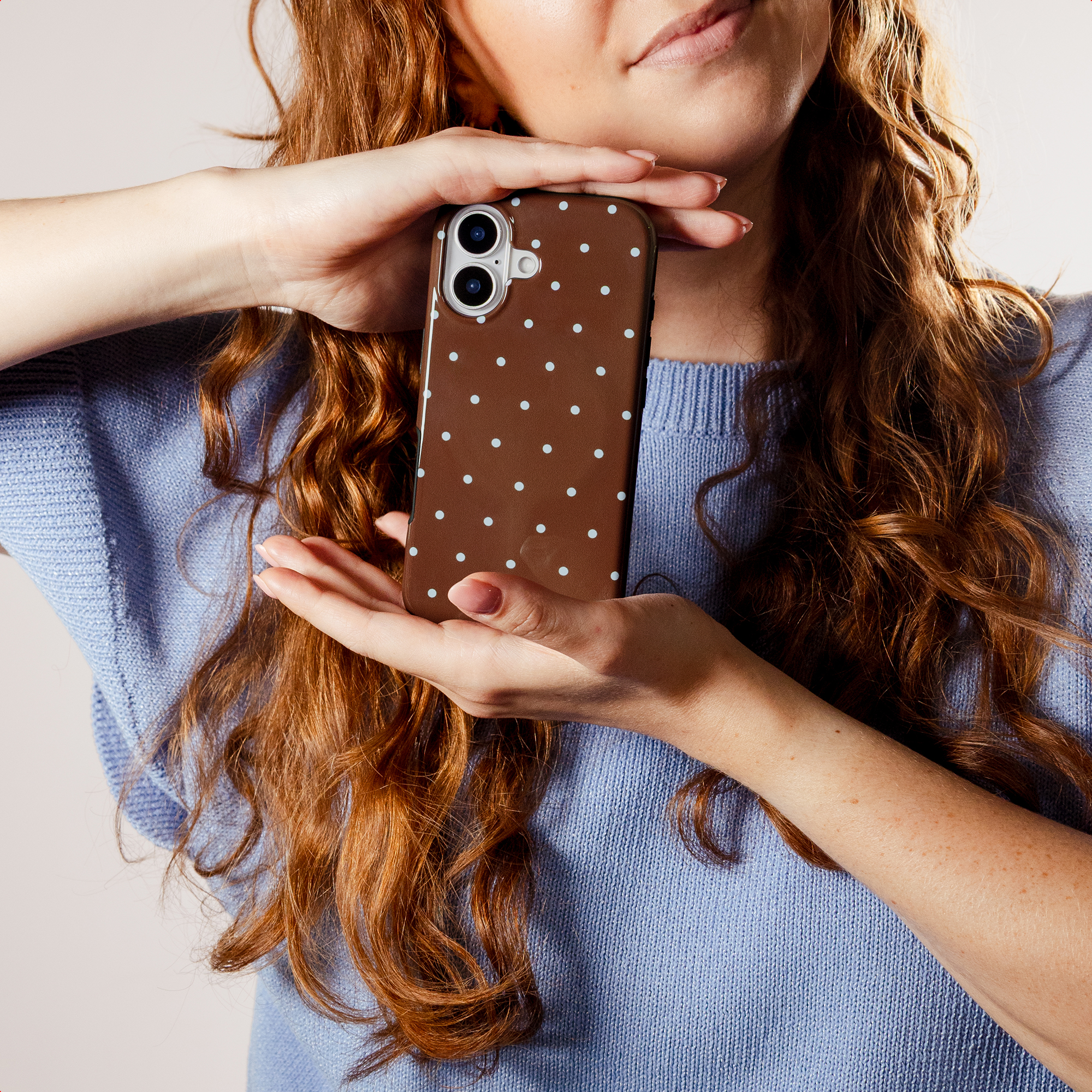 A woman with red hair holds a brown phone case with white polka dots.
