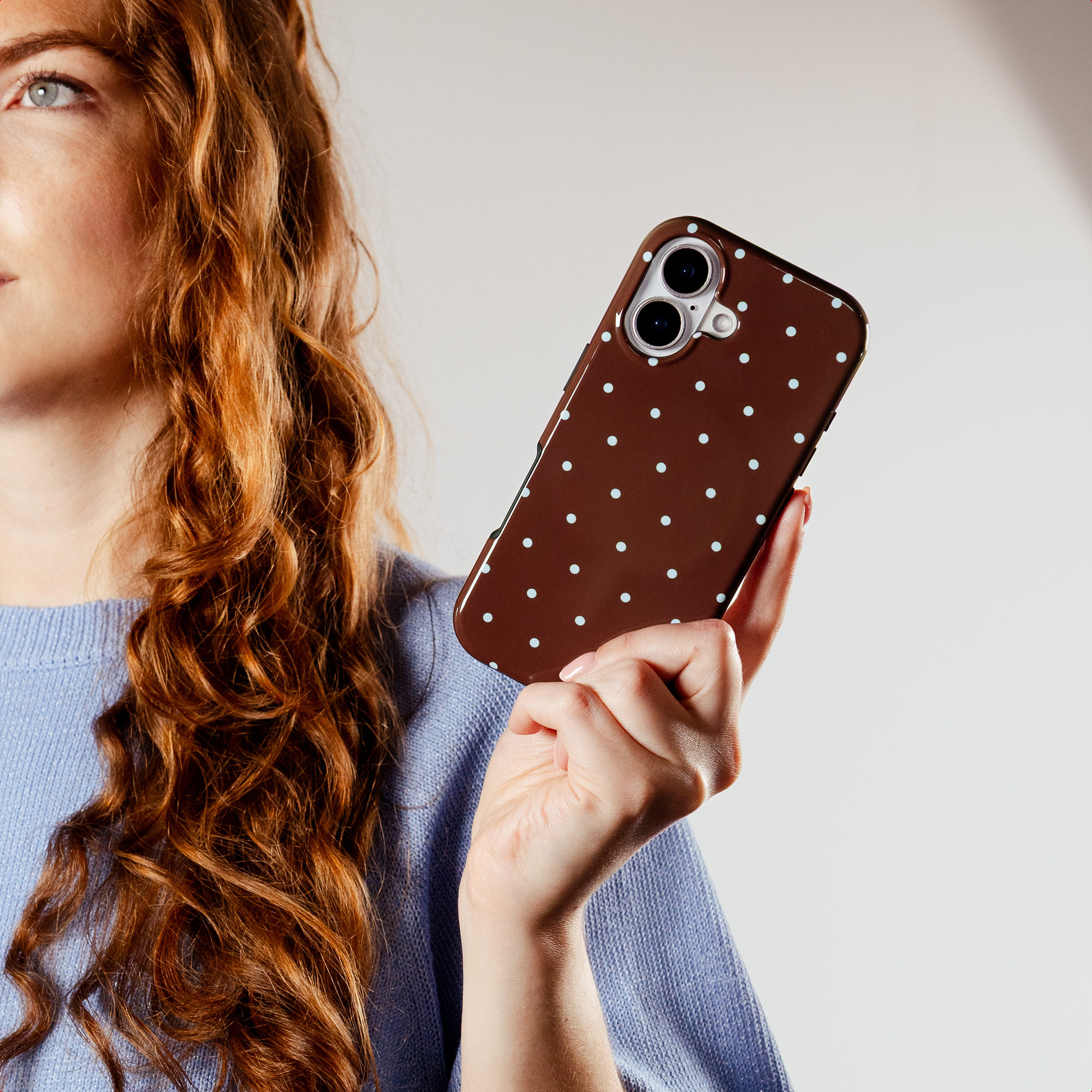 Woman with red hair holds a brown phone case with white polka dots.