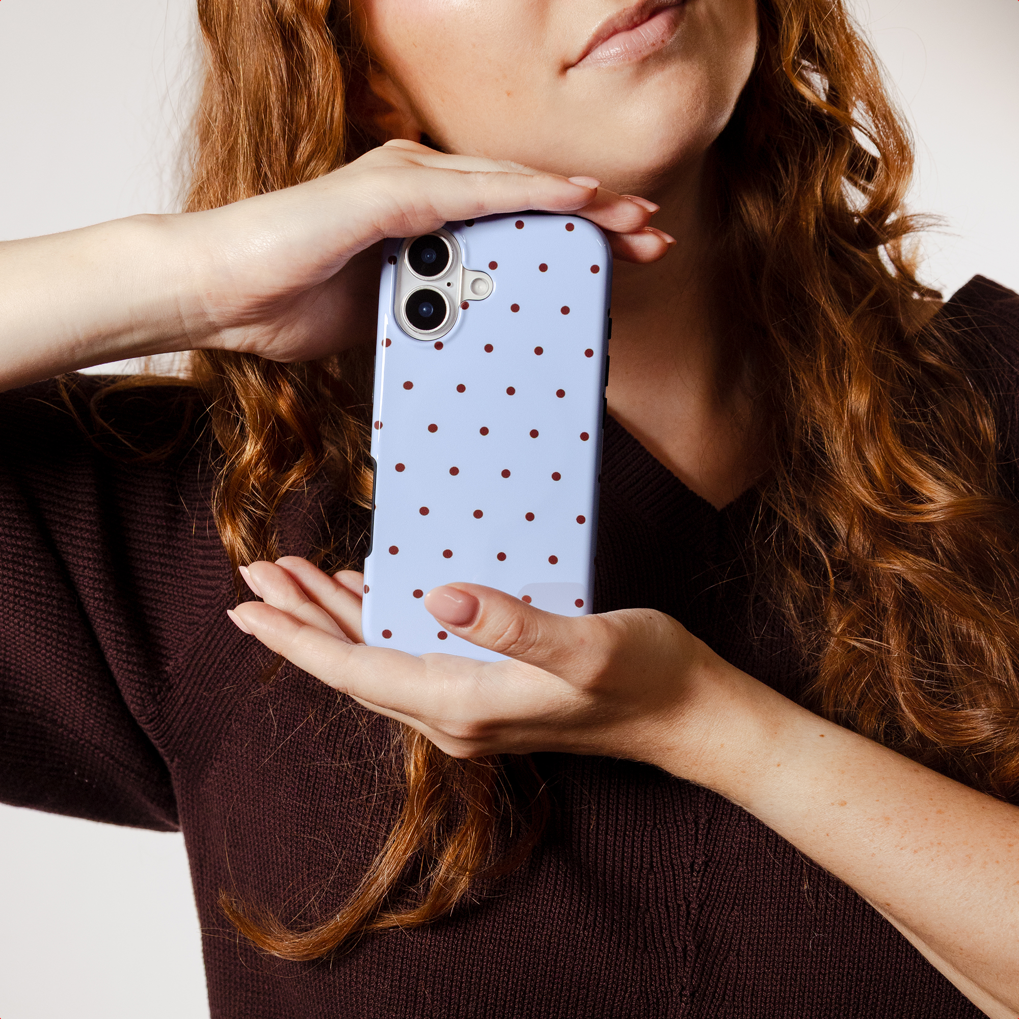 A woman with red hair holds a light blue phone case with brown dots.
