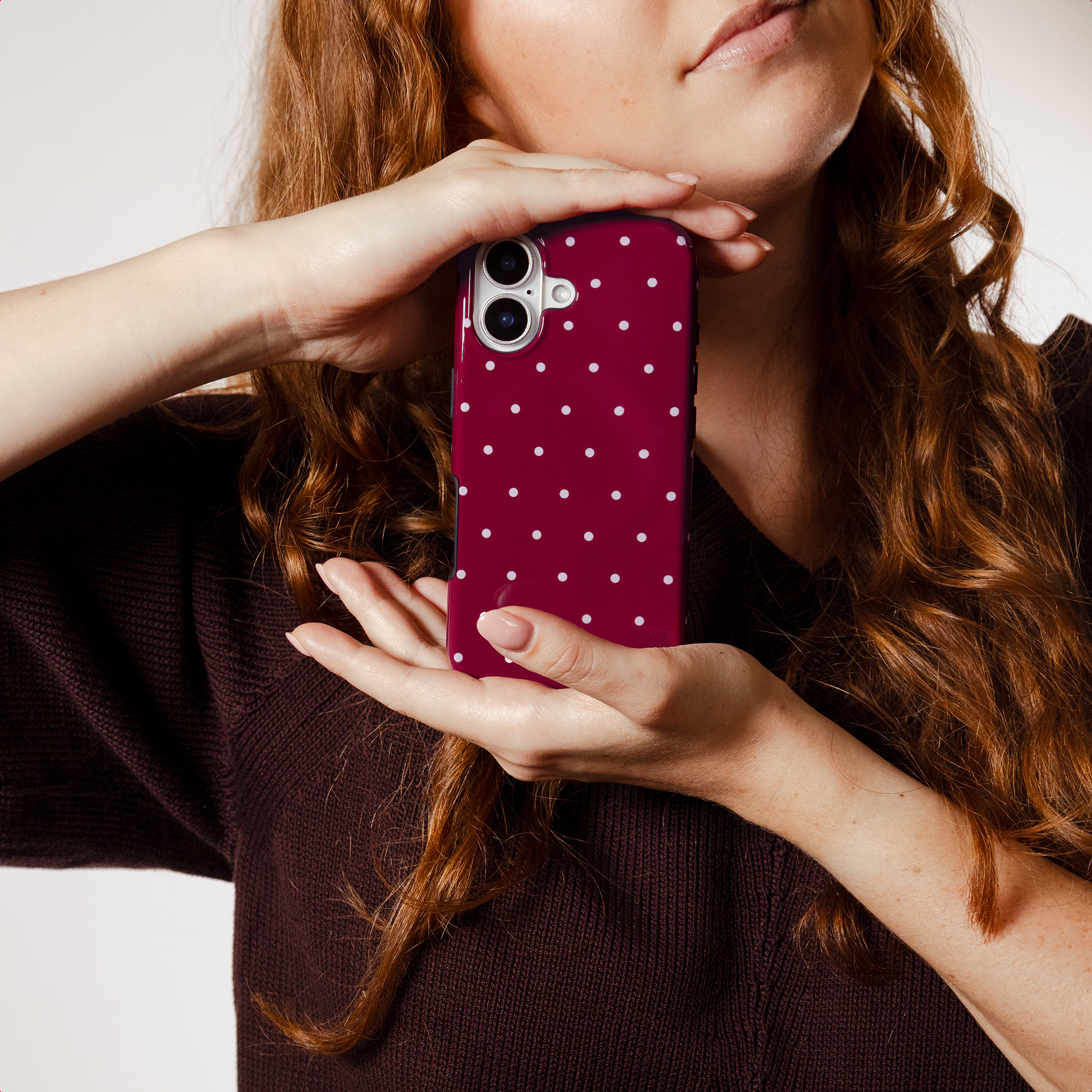 A woman with red hair holds a dark red phone case with white polka dots.