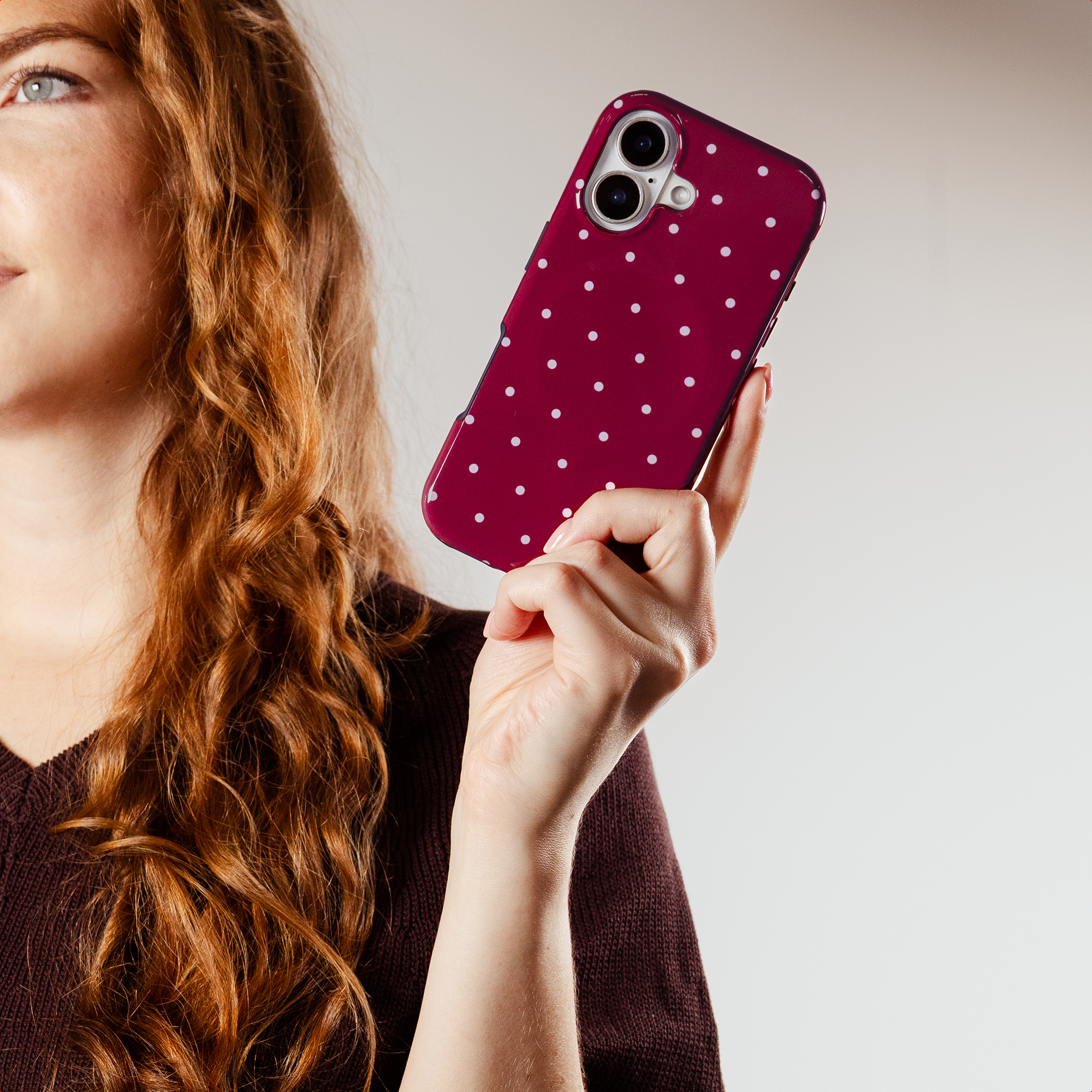 A woman with red hair holds a phone case with white polka dots.