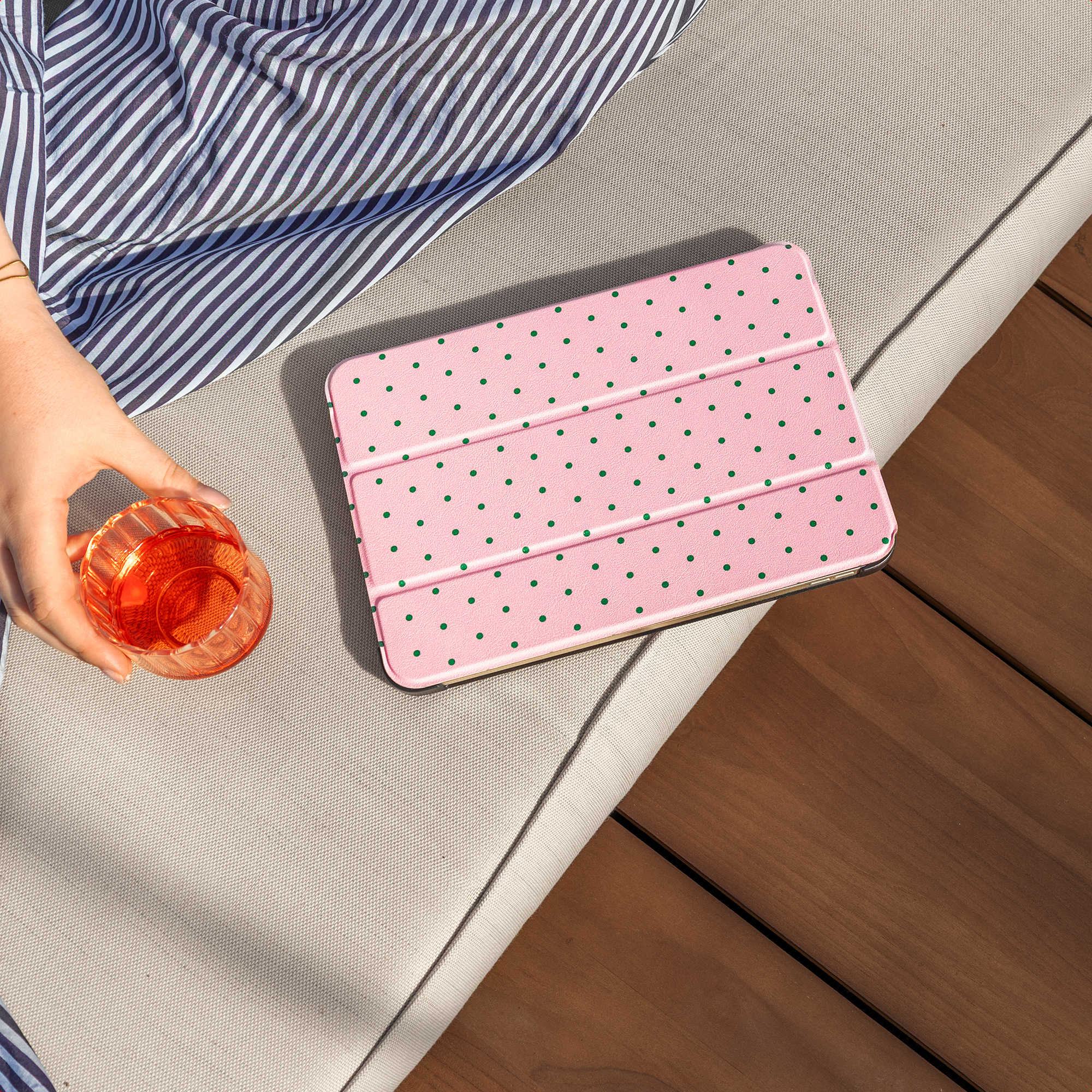 Een hand houdt een glas met oranje drankje vast naast een roze tablethoes.