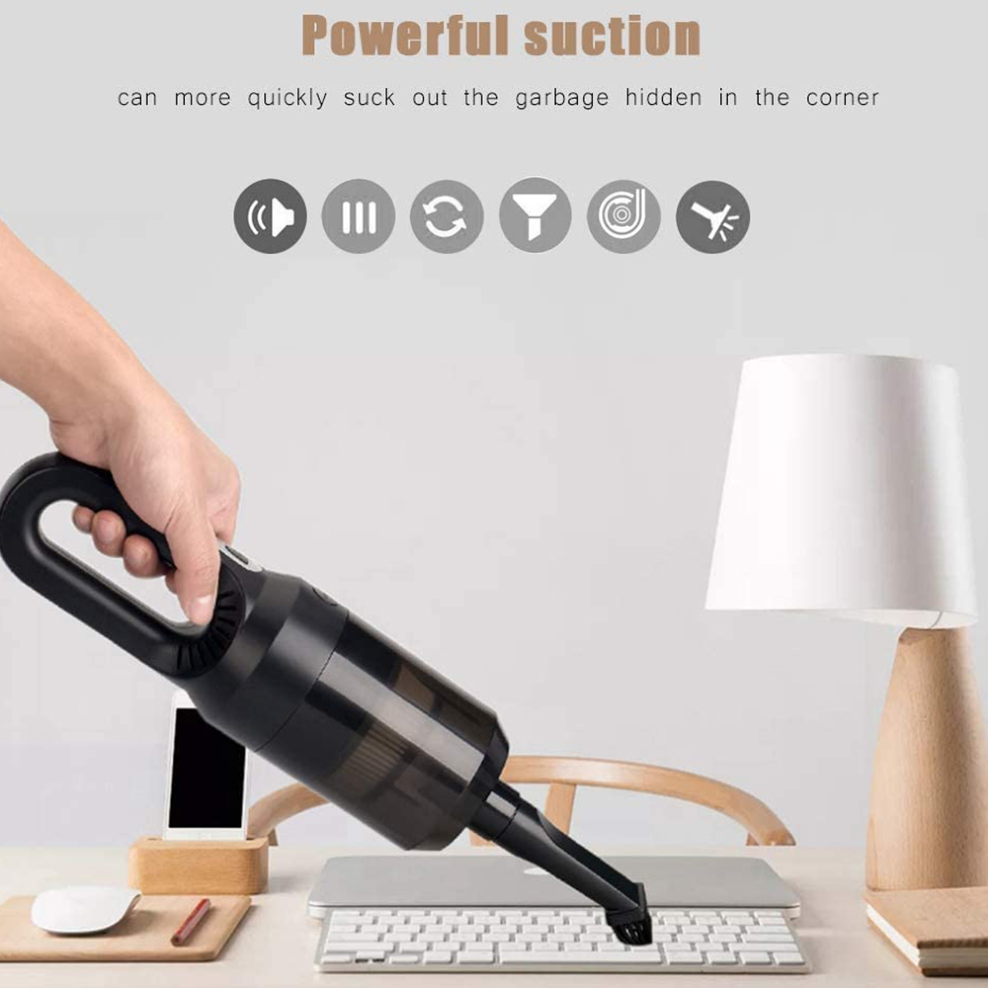 Hand hält schwarzen Staubsauger über Tastatur. Schreibtisch mit Lampe im Hintergrund.