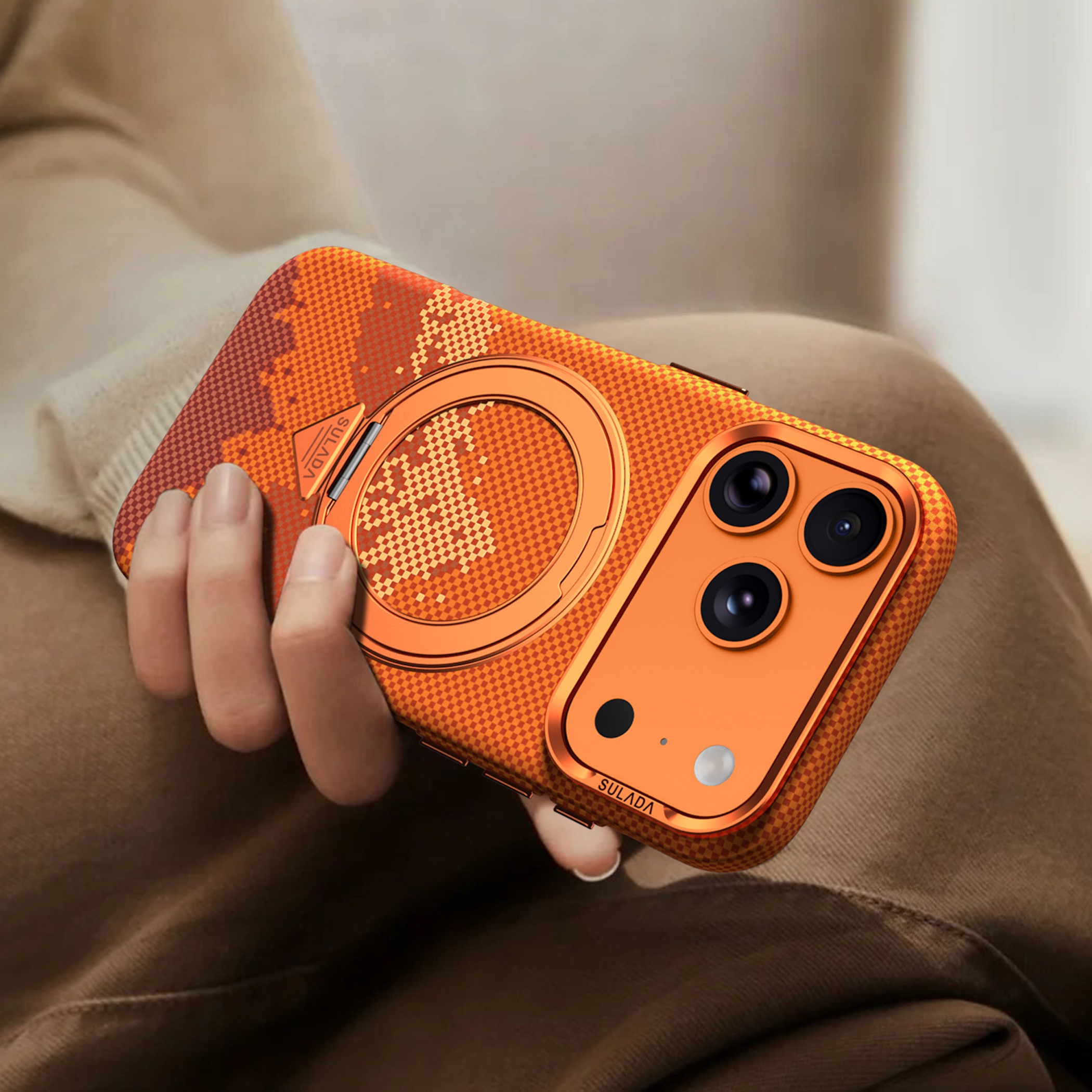 Eine Hand hält ein orangefarbenes Handy mit einem karierten Muster und Kameramodul.