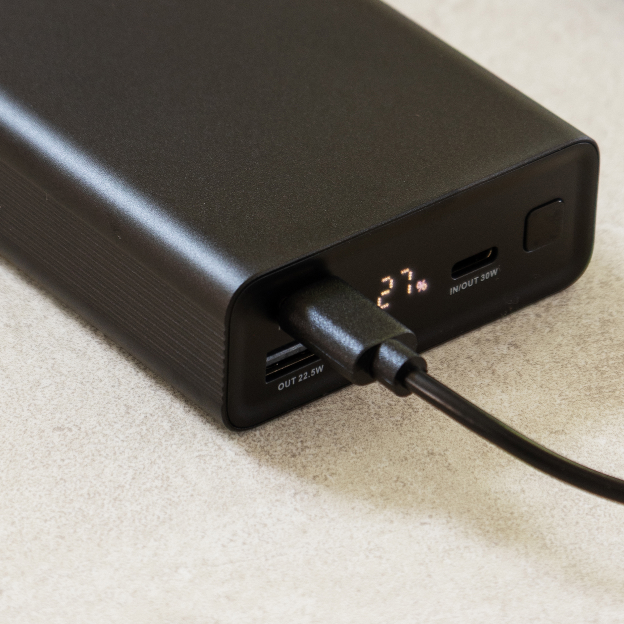 Power bank nera mostra 27% di carica, con porta USB-C e cavo nero.
