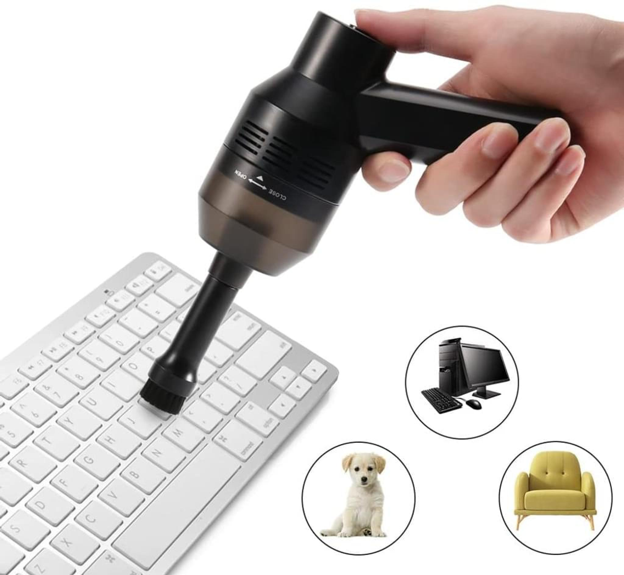 Eine Hand hält einen schwarzen Mini-Staubsauger über einer weißen Tastatur. Daneben sind ein Computer, ein Hundewelpe und ein Sessel zu sehen.