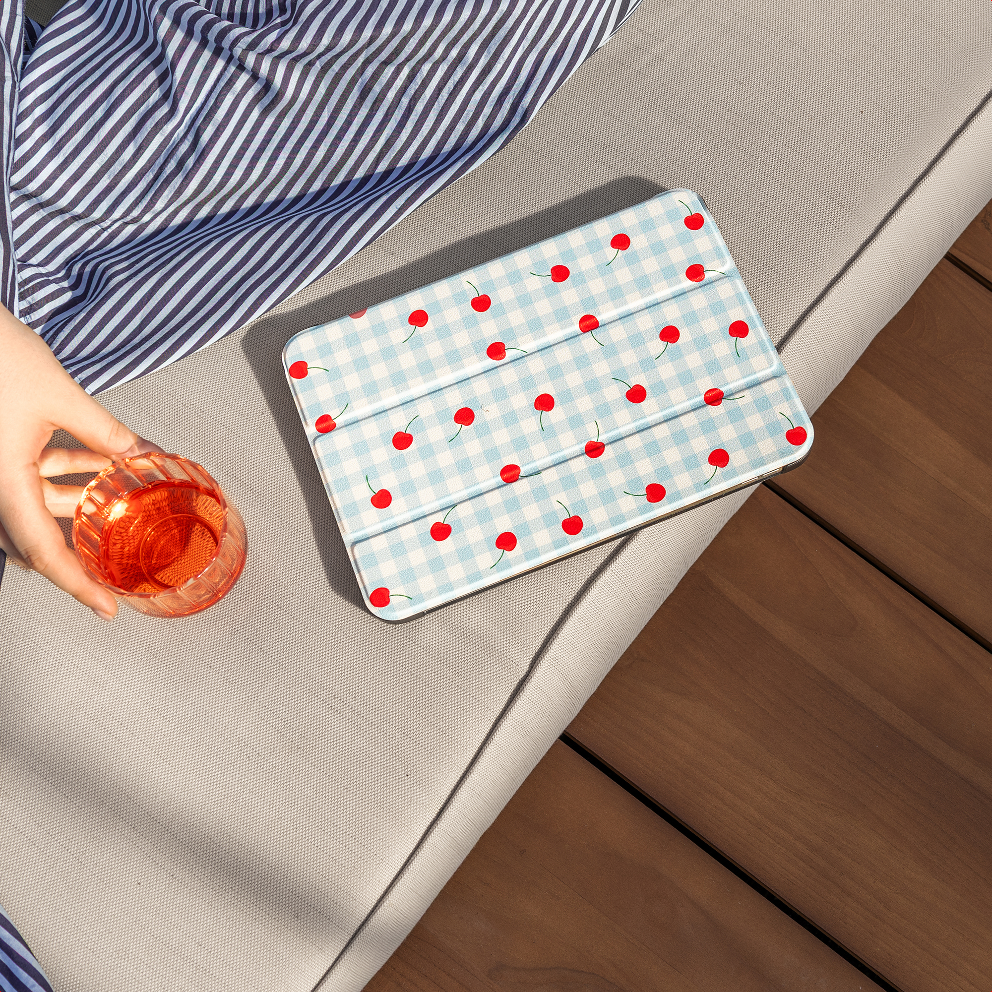 Een hand houdt een glas met oranje drank vast naast een tablethoes met kersenpatroon.