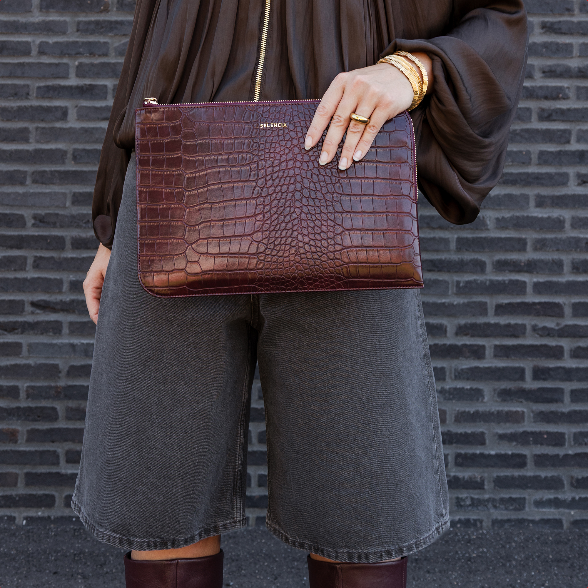 Person mit brauner Kroko-Clutch, grauer Denim-Shorts und hohen Stiefeln.