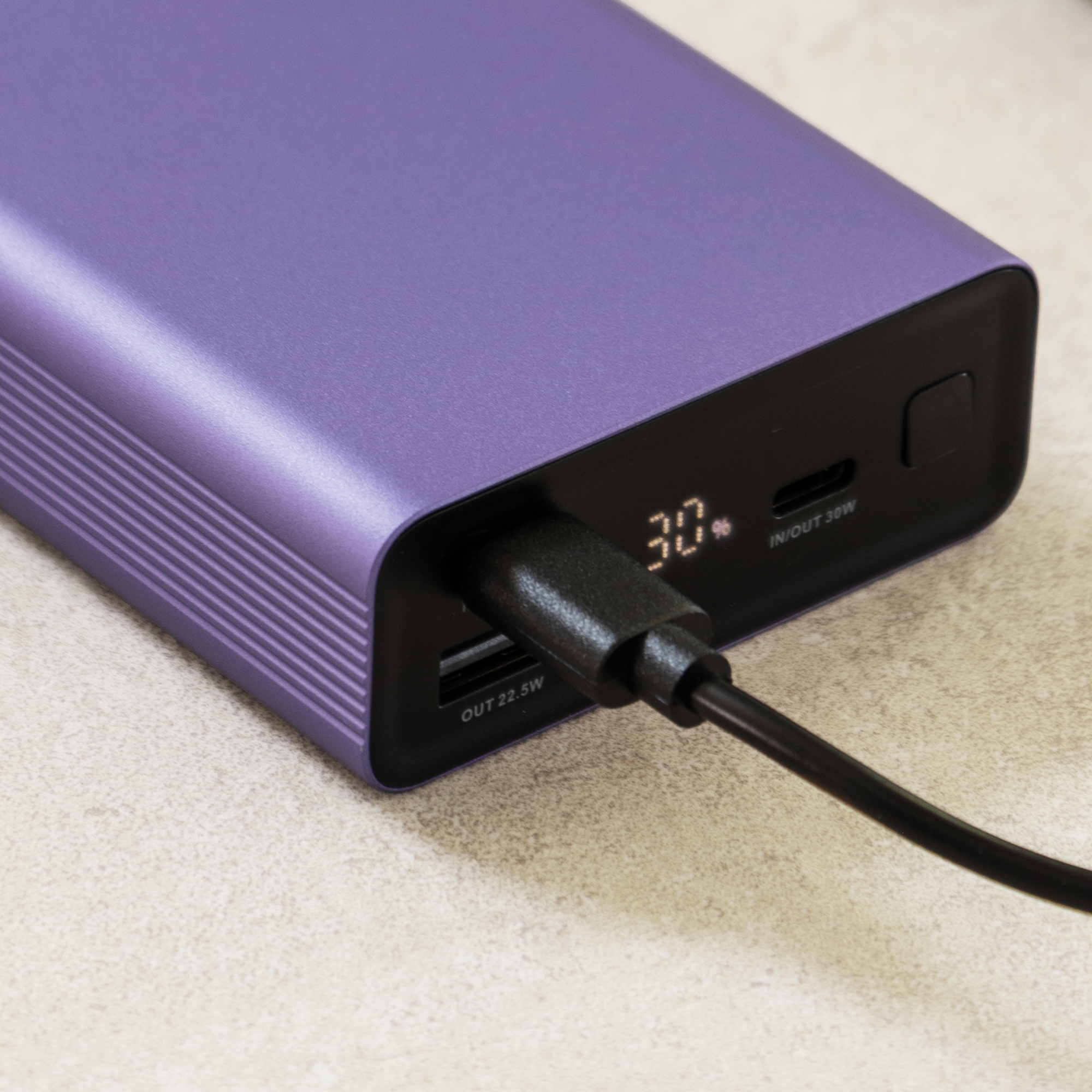 A purple power bank showing 30% charge, with a USB cable plugged in.