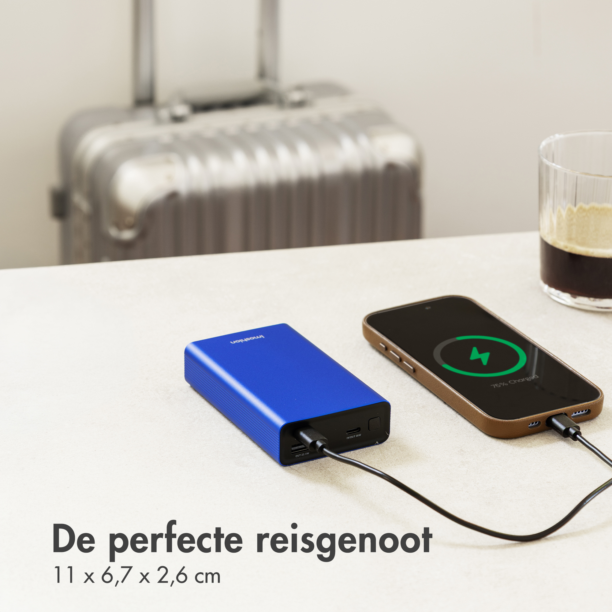 Blue power bank charging a smartphone. Suitcase & glass in background.