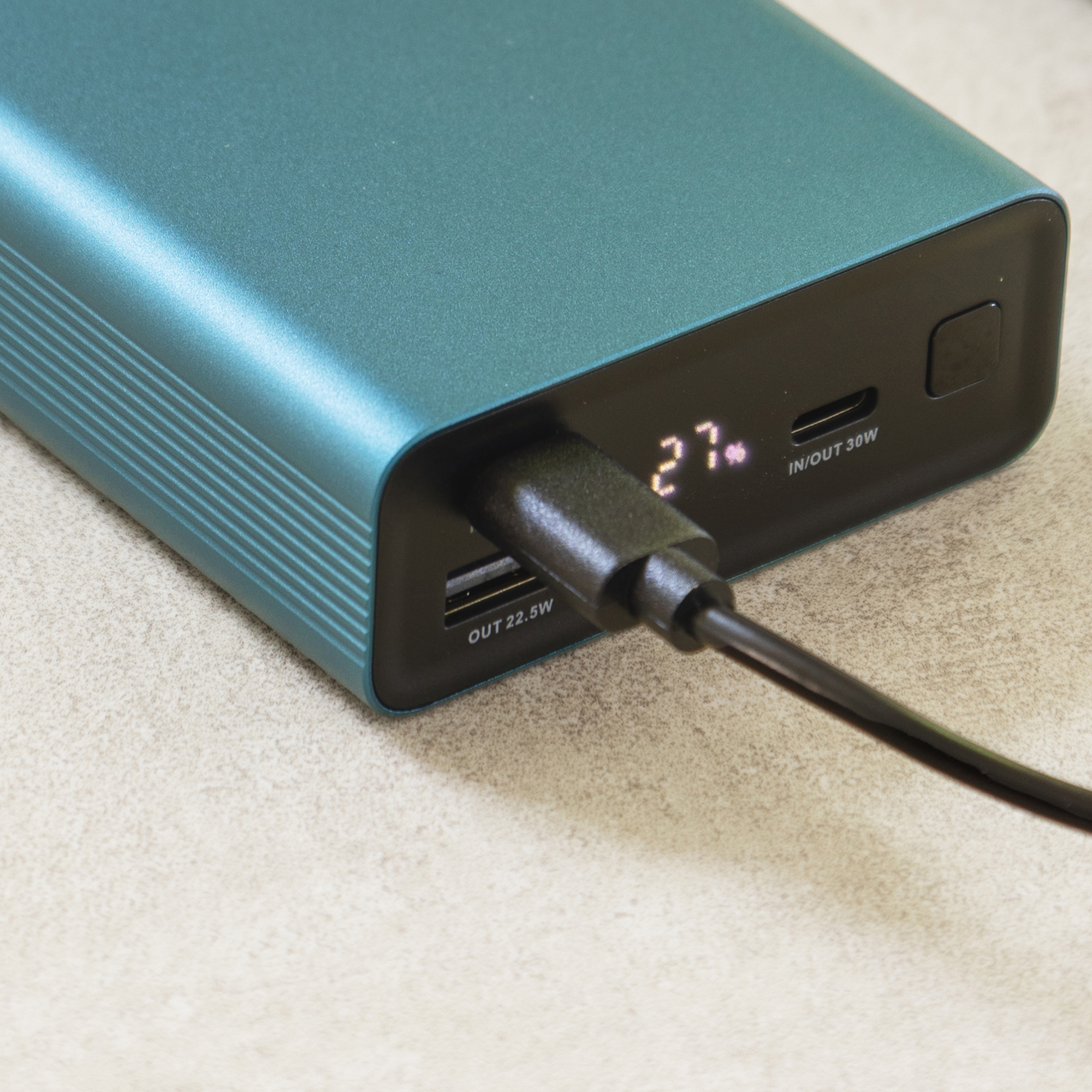 Un power bank verde acqua con cavo collegato. Lo schermo mostra il 27%.
