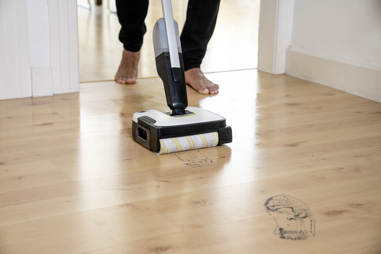 Un mocio umido pulisce un pavimento in legno con impronte visibili.