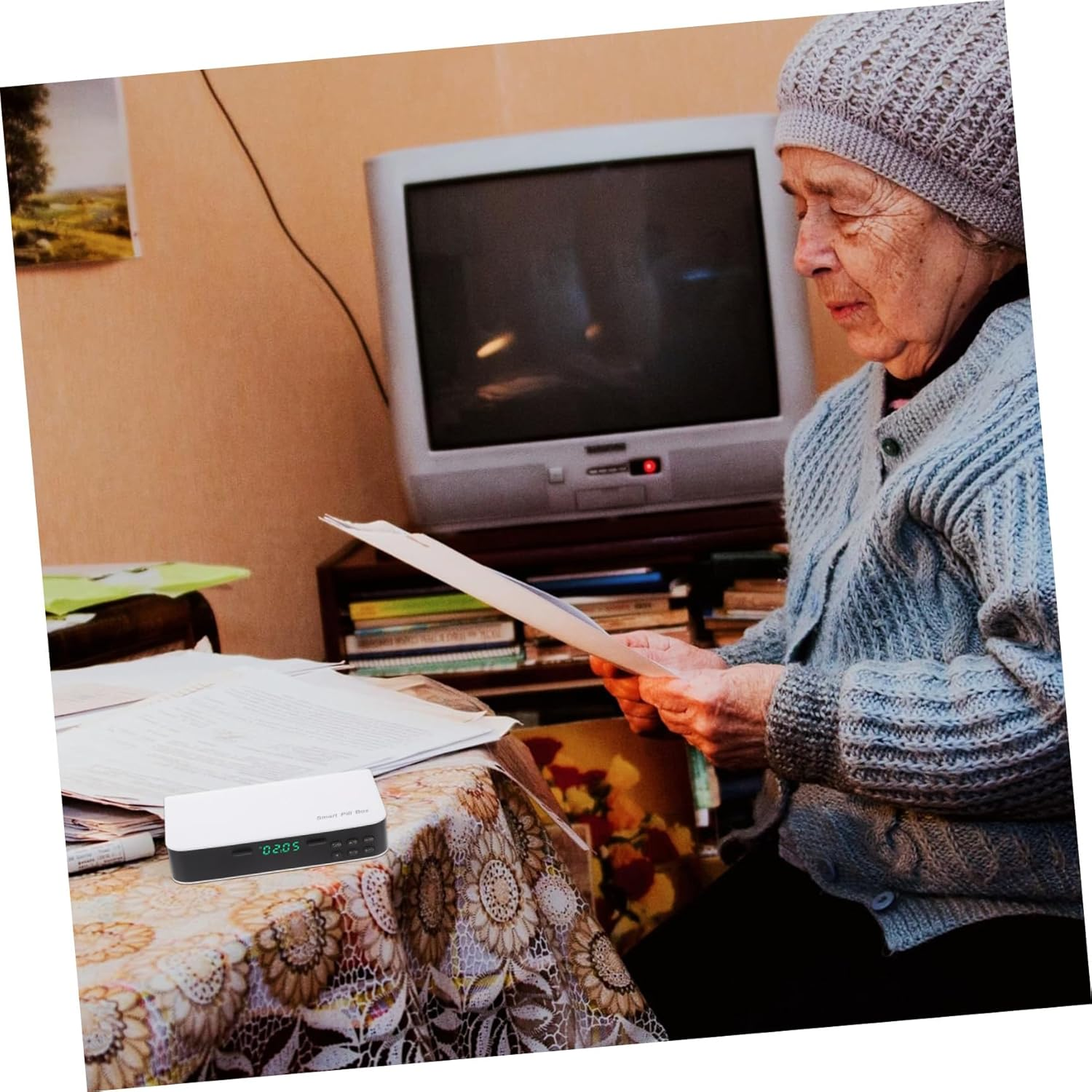 Eine ältere Frau mit Mütze liest Dokumente vor einem Fernseher und einem kleinen Kasten.