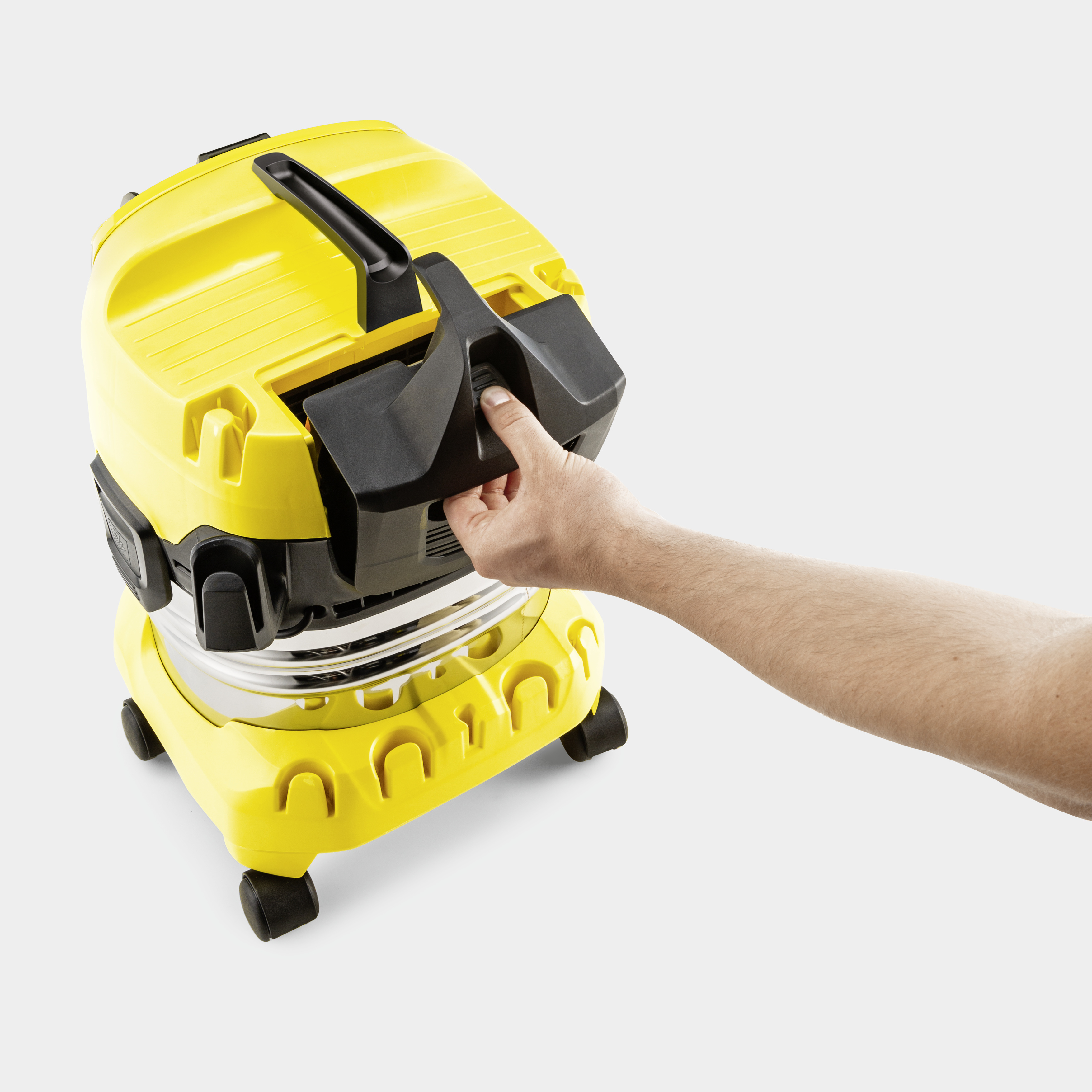 Una mano preme un pulsante nero su un aspirapolvere giallo.