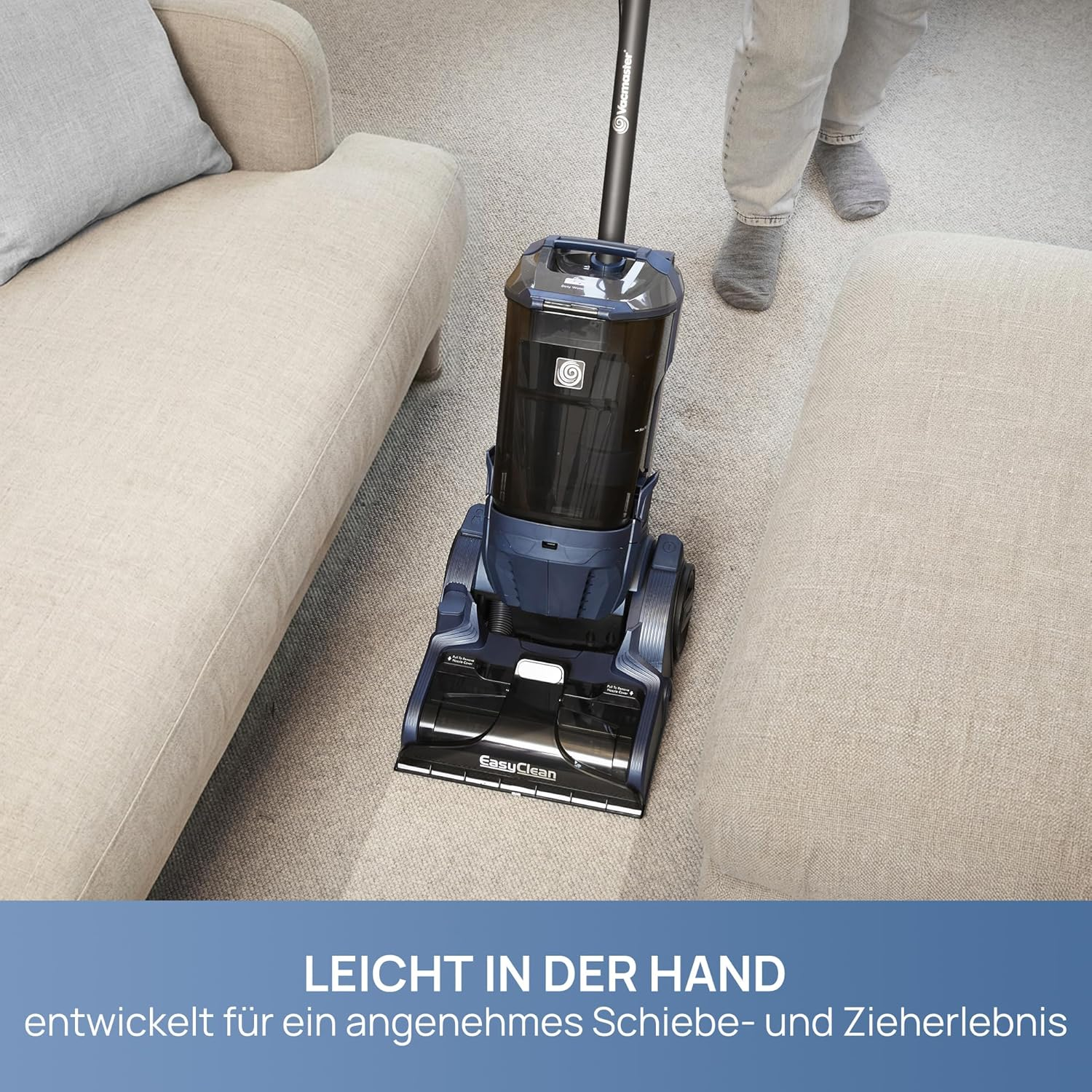Ein blauer Staubsauger wird auf einem hellen Teppich neben einem Sofa benutzt.