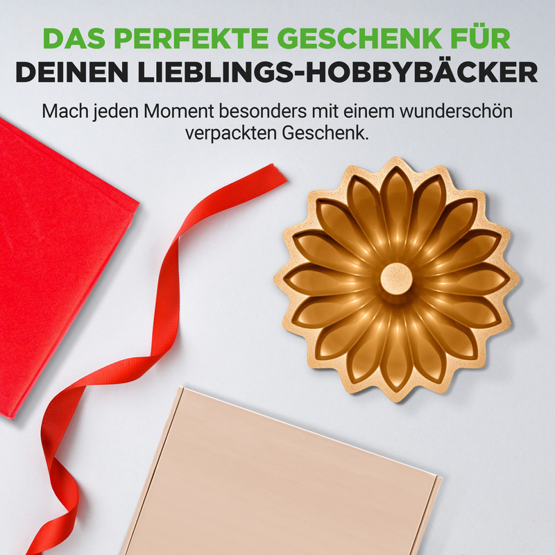 Goldene Kuchenform in Blumenform neben roten Geschenkpapier und Band.
