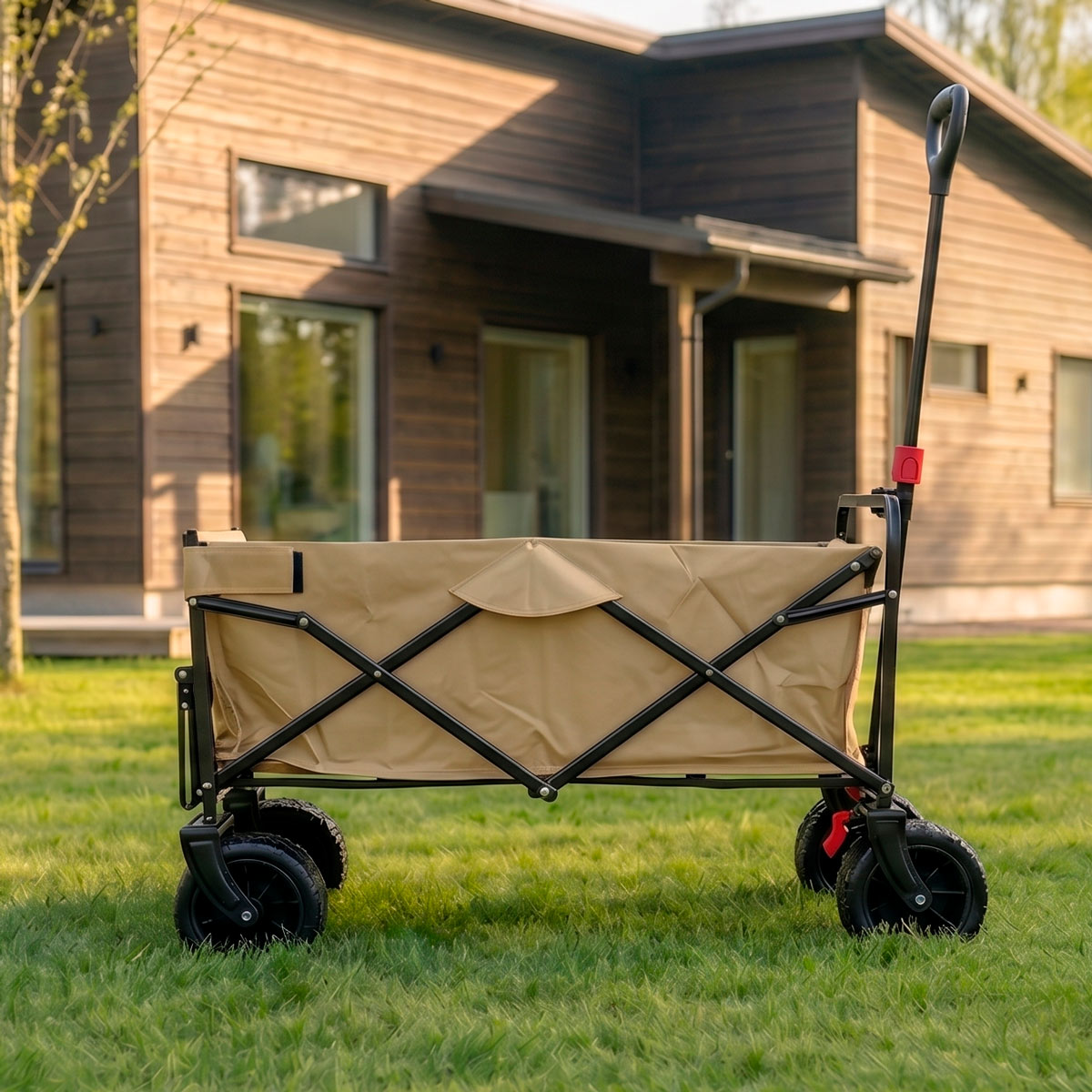 Ein beige Stoffwagen mit schwarzem Rahmen und Rädern steht auf grünem Gras vor einem Holzhaus.