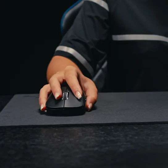 La mano di una persona che tiene un mouse nero su un tappetino grigio scuro.