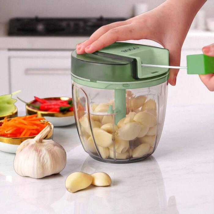 Una mano tira la maniglia di un tritacarne per aglio verde riempito con spicchi d'aglio interi.