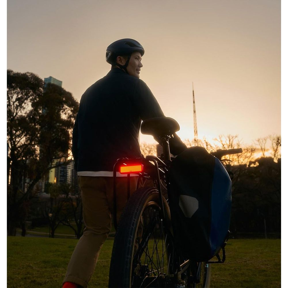 Mann mit Helm steht bei Sonnenuntergang im Park neben Fahrrad mit Packtasche.