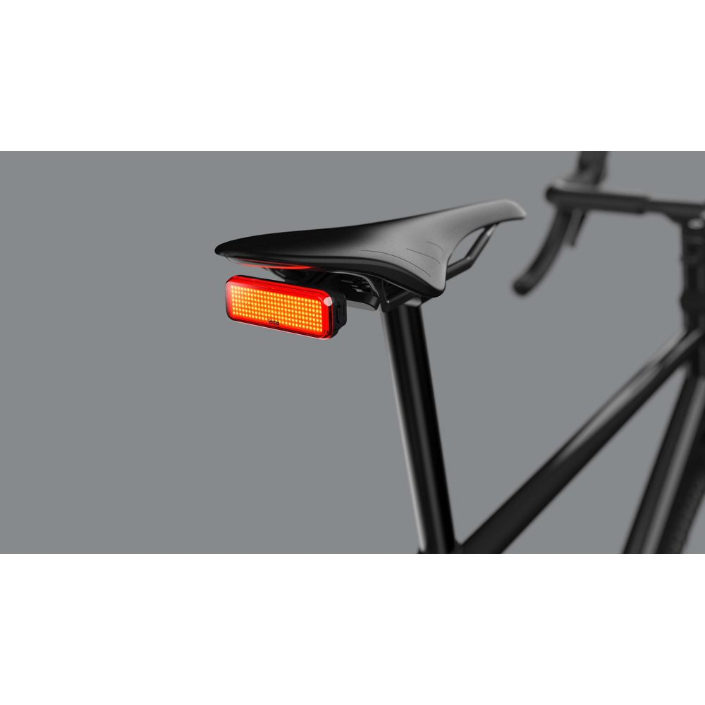 Rücklicht an einem schwarzen Fahrradsattel auf grauem Hintergrund.