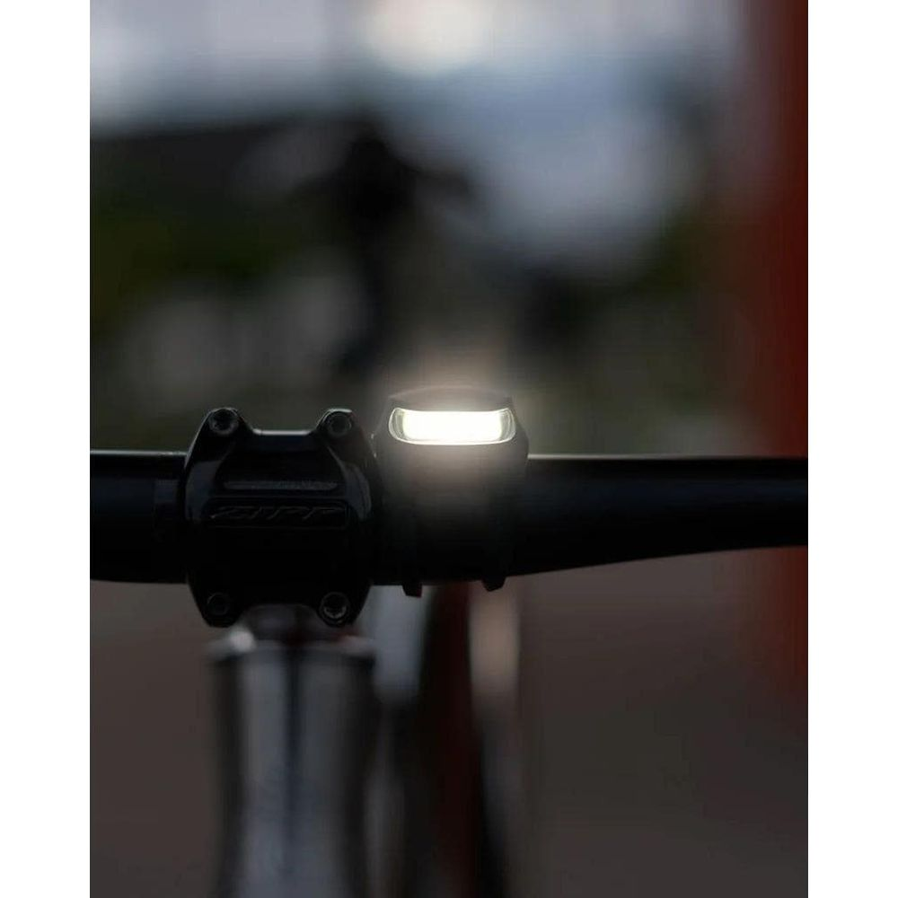Ein helles Fahrradlicht leuchtet auf einem schwarzen Lenker mit unscharfem Hintergrund.