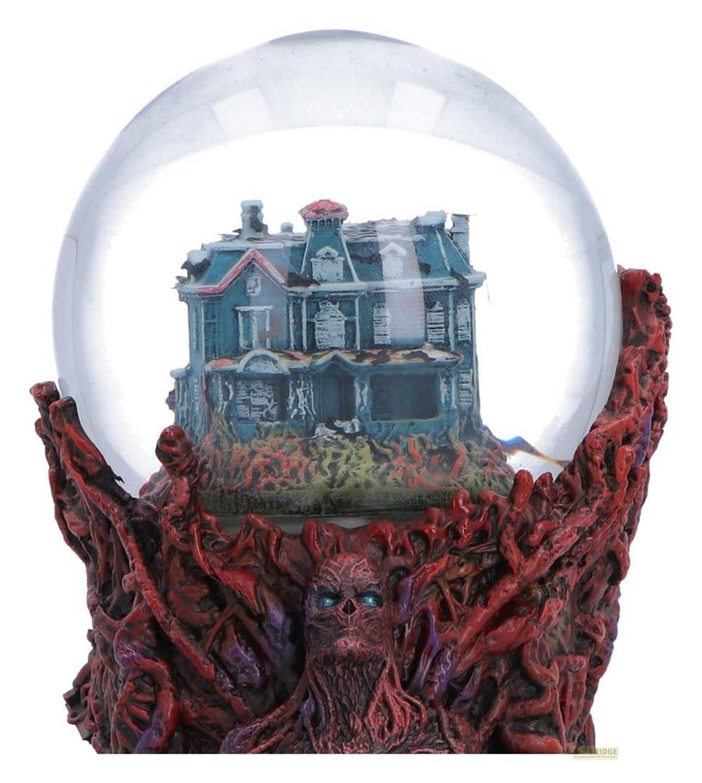 Ein verwittertes Haus in einem Schneeball auf einem roten Sockel mit einem dämonischen Gesicht.