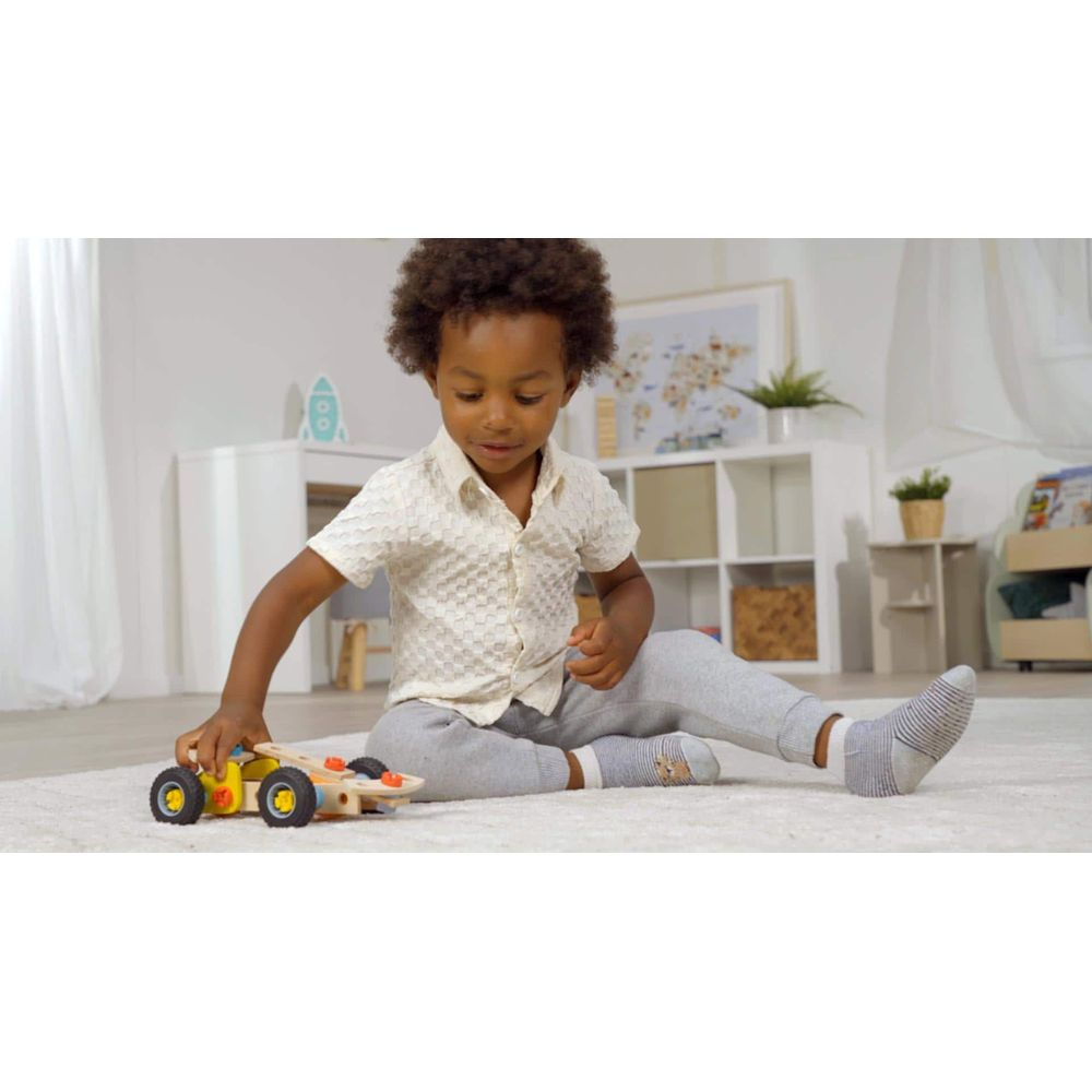 Ein kleiner Junge spielt mit einem Holzauto auf einem Teppich im Kinderzimmer.
