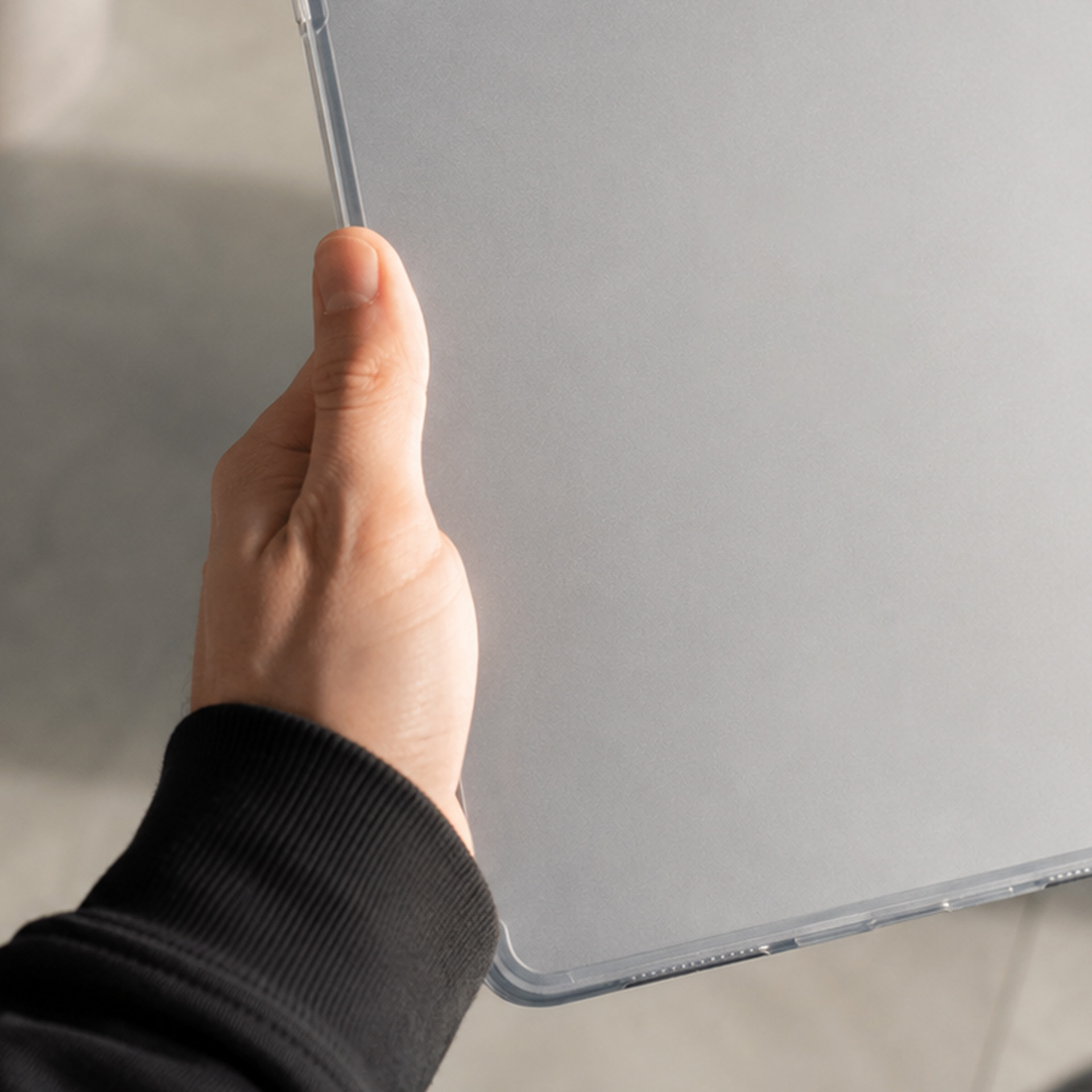 Dłoń trzyma srebrny tablet w przezroczystym etui.