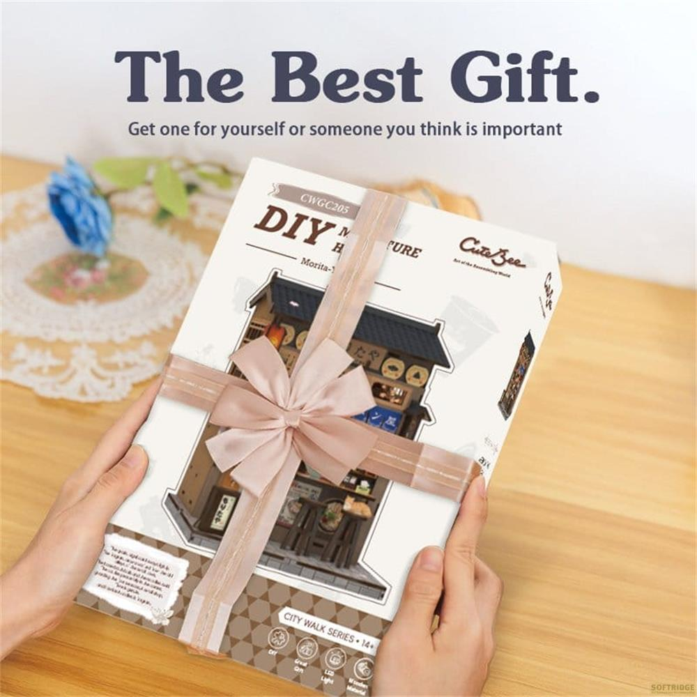 Hände halten eine Geschenkbox mit rosa Band, die ein DIY-Miniaturhaus-Kit zeigt.