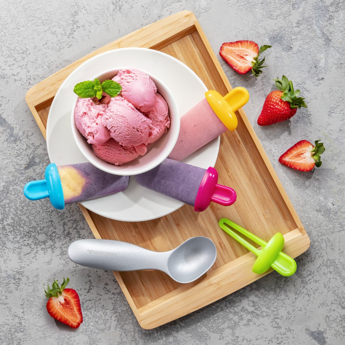 Gelato rosa in una ciotola, ghiaccioli e fragole su un vassoio di legno.